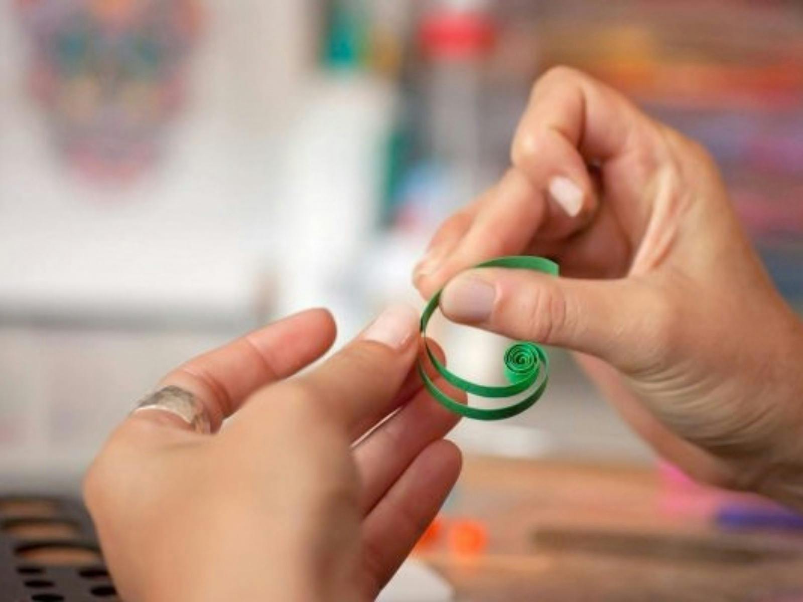 Two hands in the shot holding pieces of green curled paper being glued together.