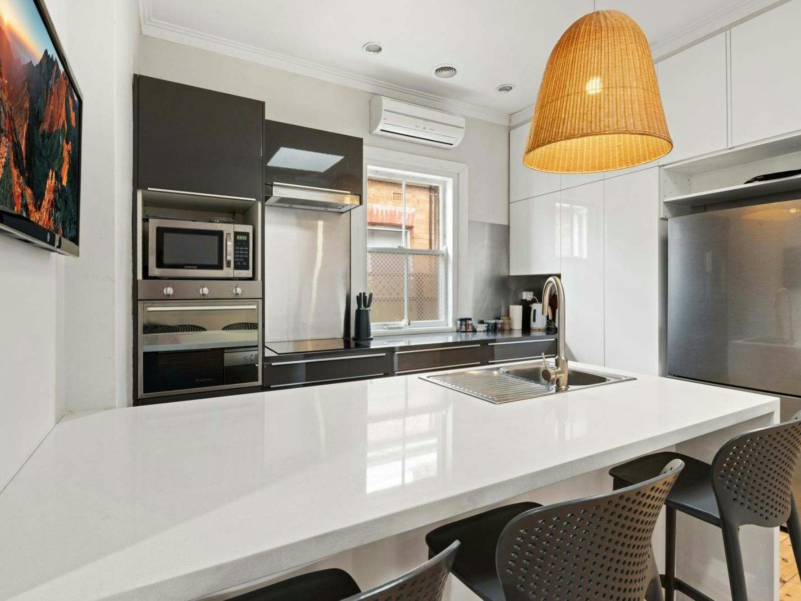Kitchen with white and black cabinets and white bench top, wicker pendant light above the bench