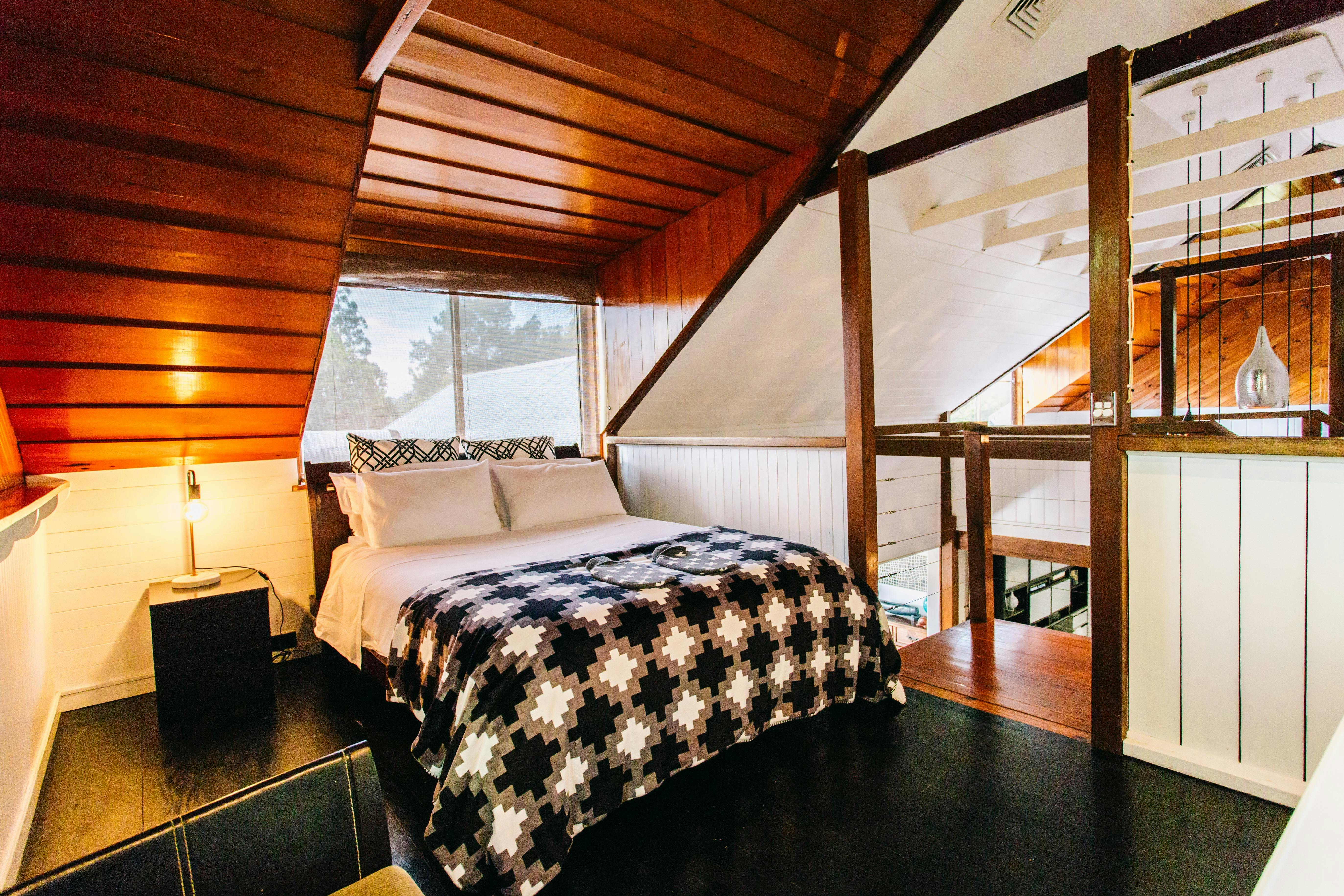 Queen size bed in Loft #1 with dormer windows. Open plan. Light on side table at Bellingen Converted