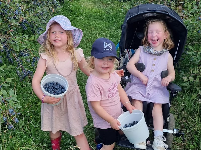 Three happy children, two holding buckets of berries and one in a wheelchair