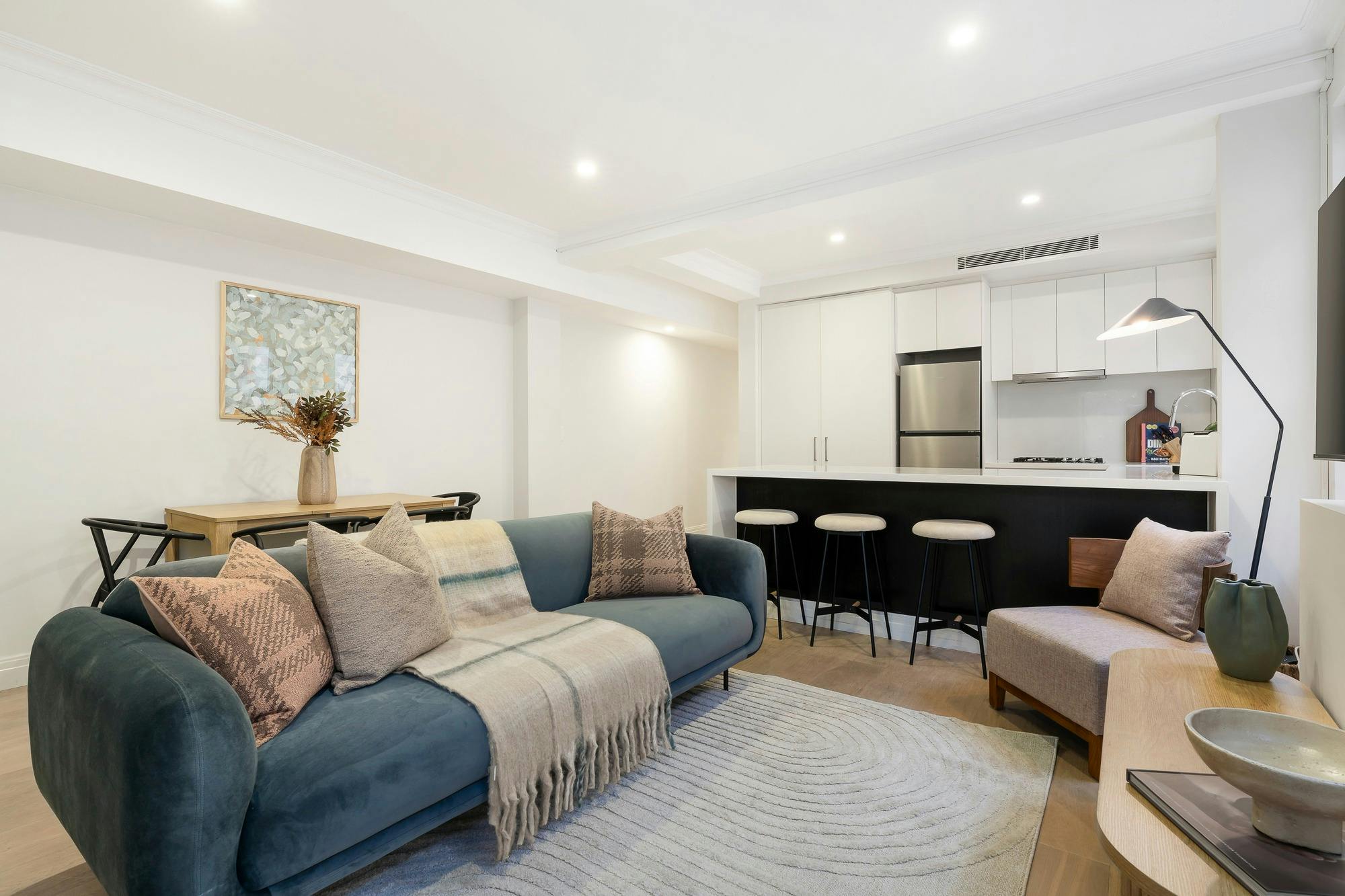 Spacious, modern, open plan living room with blue couch, dining table and kitchen island bench.