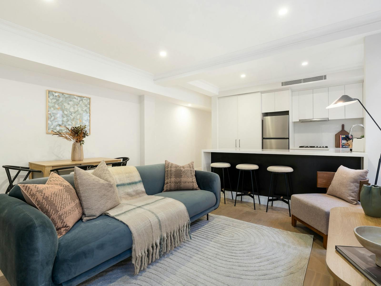 Spacious, modern, open plan living room with blue couch, dining table and kitchen island bench.