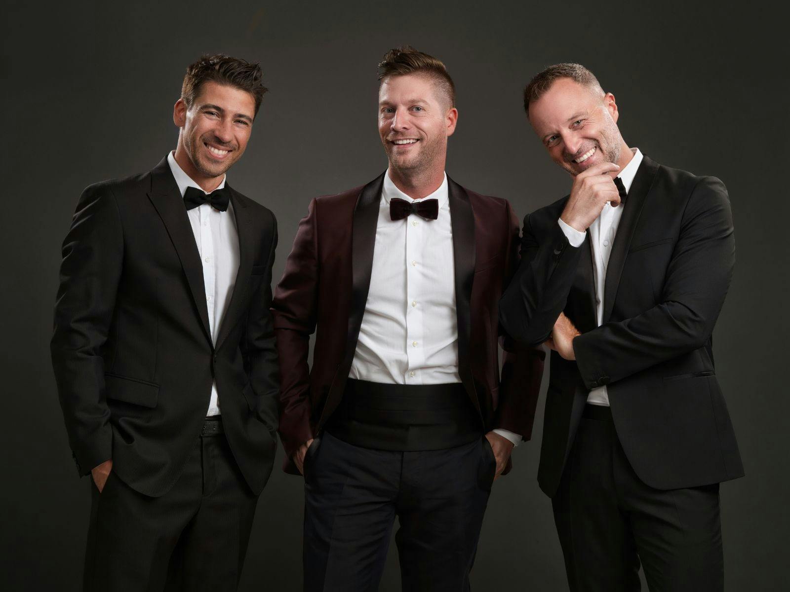 Three men in suits standing and smiling in the direction of the camera