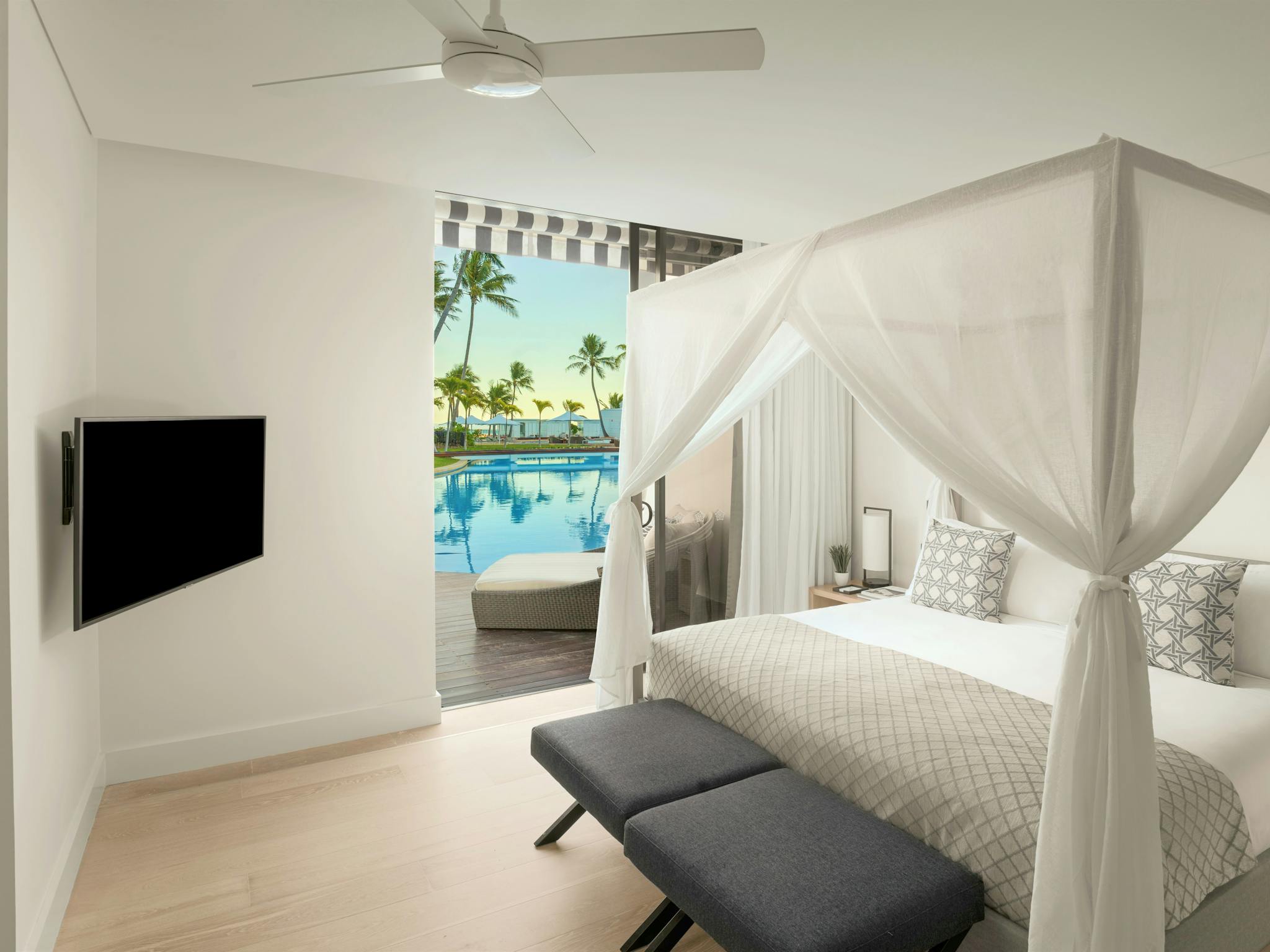 A bedroom featuring a canopy bed, modern decor, and direct access to a poolside deck with palm trees A bedroom featuring a canopy bed, modern decor, and direct access to a poolside deck with palm trees