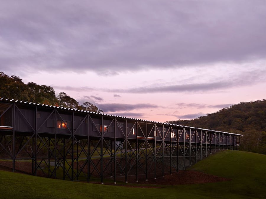 A twilight image of The Bridge, a long and narrow timber building spanning a grassy gully