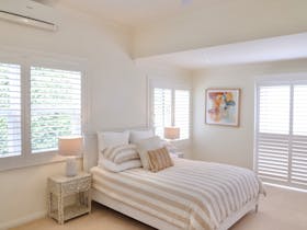 Queen bedroom with bedside tables, lamps and plantation shutters.