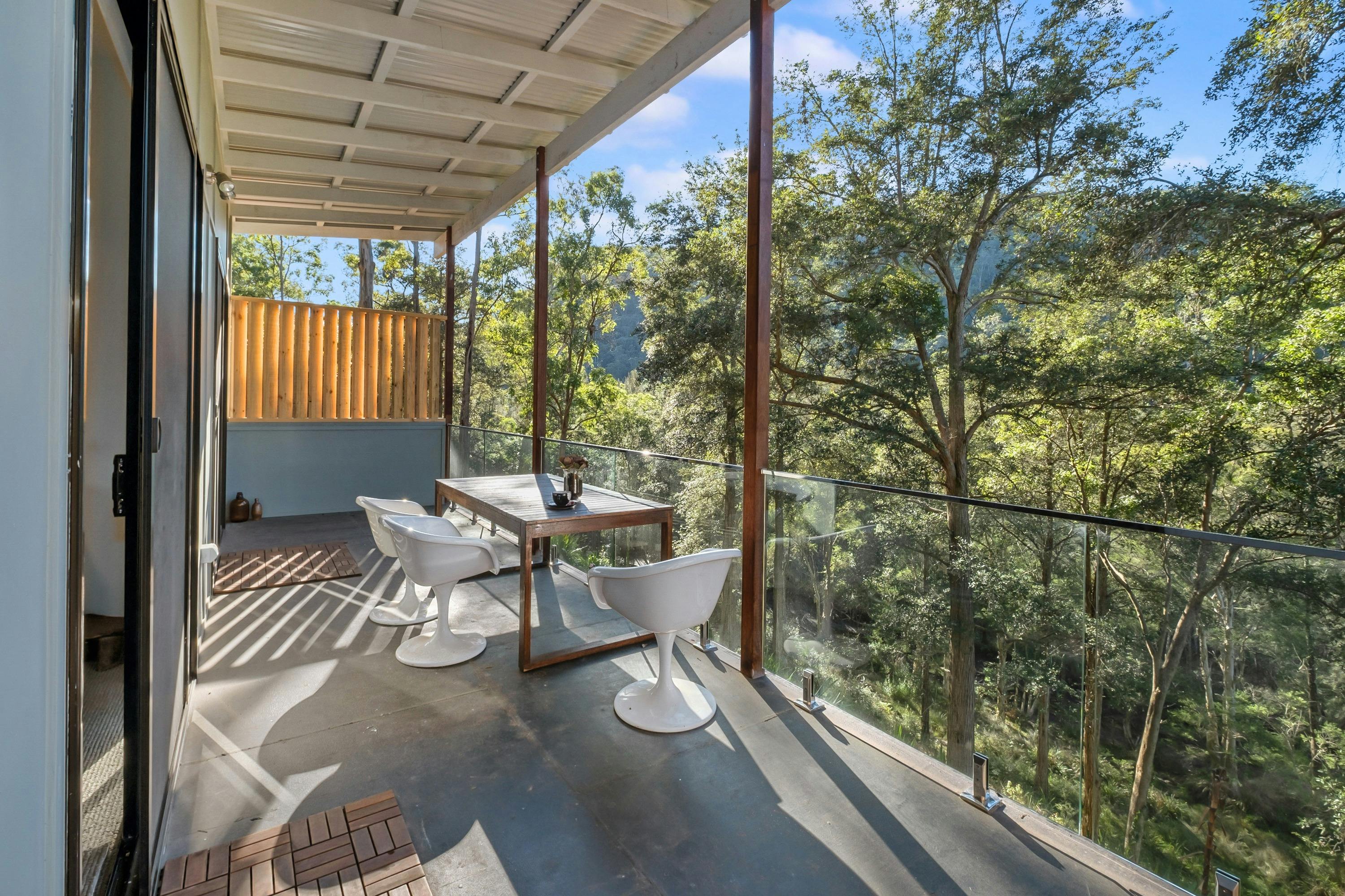 Outdoor deck at Gymea Cottage with a table and chairs overlooking the surrounding natural landscape.