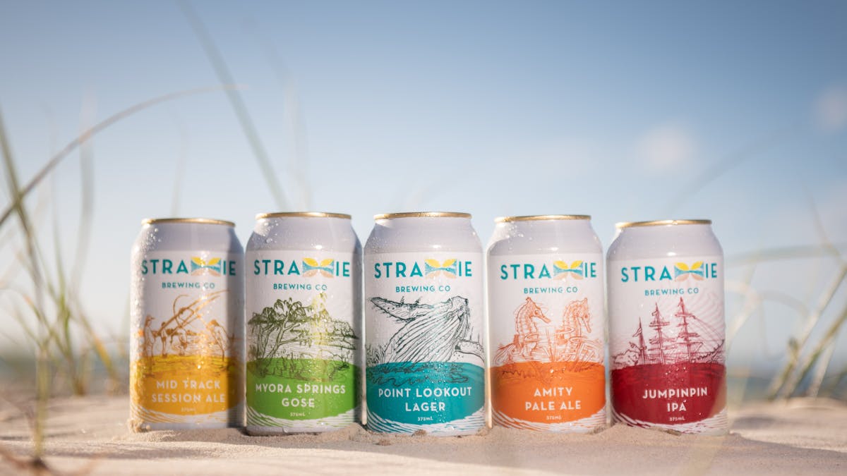 Line up of 5 of Straddie Brewing Beers on a beach