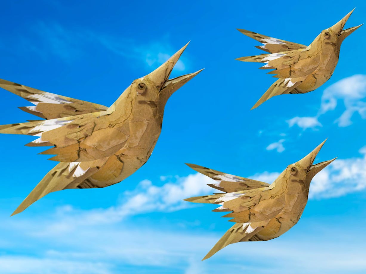 Three cardboard birds soar across a bright blue sky with soft clouds in the background.