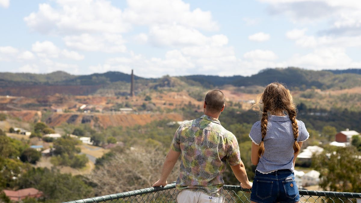 Young man and woman facing their backs to the camera looking at a view of Mount Morgan.
