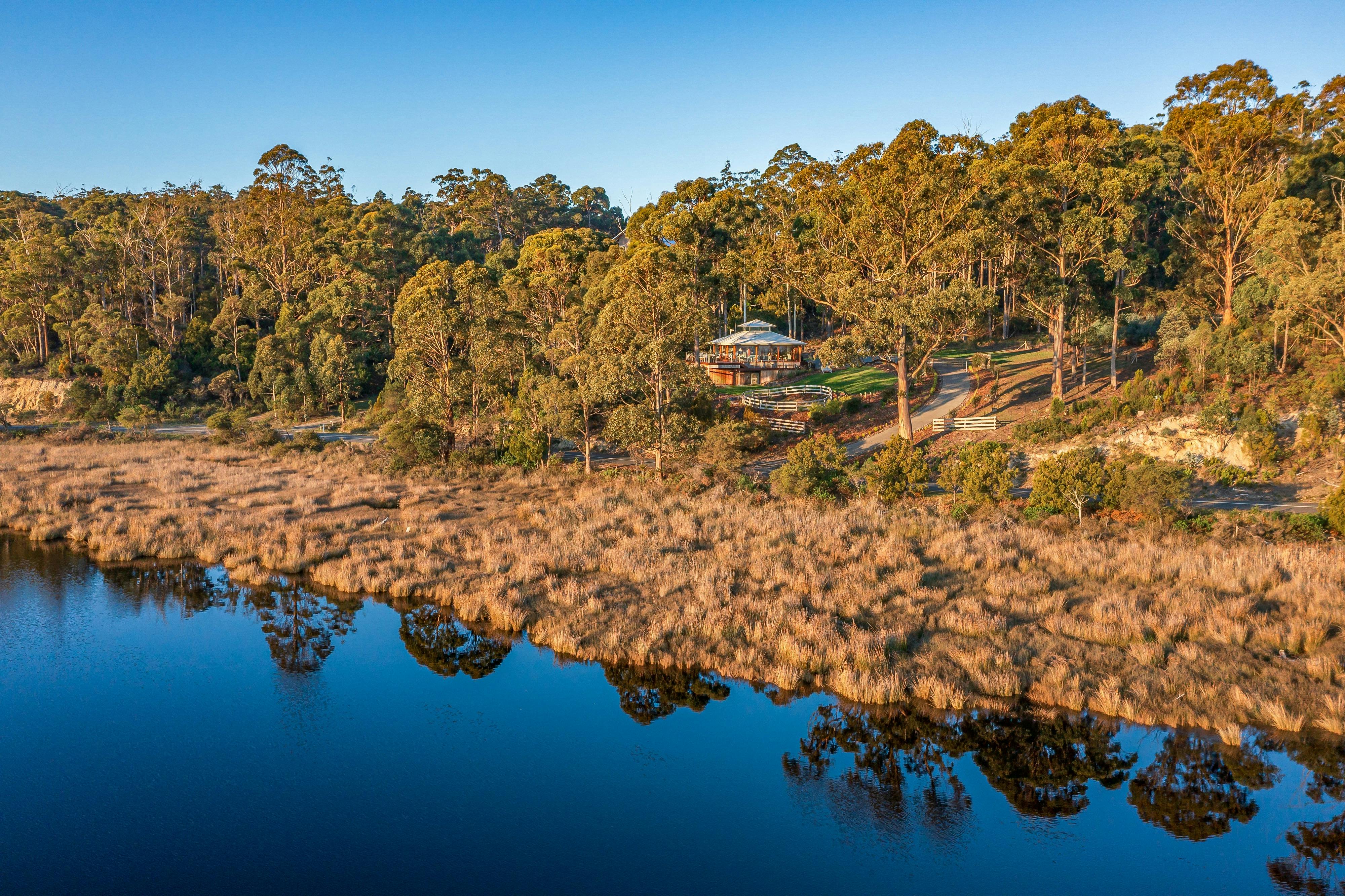 A panoramic drone shot of the Huon River Hideaway property take from above a reflective Huon River