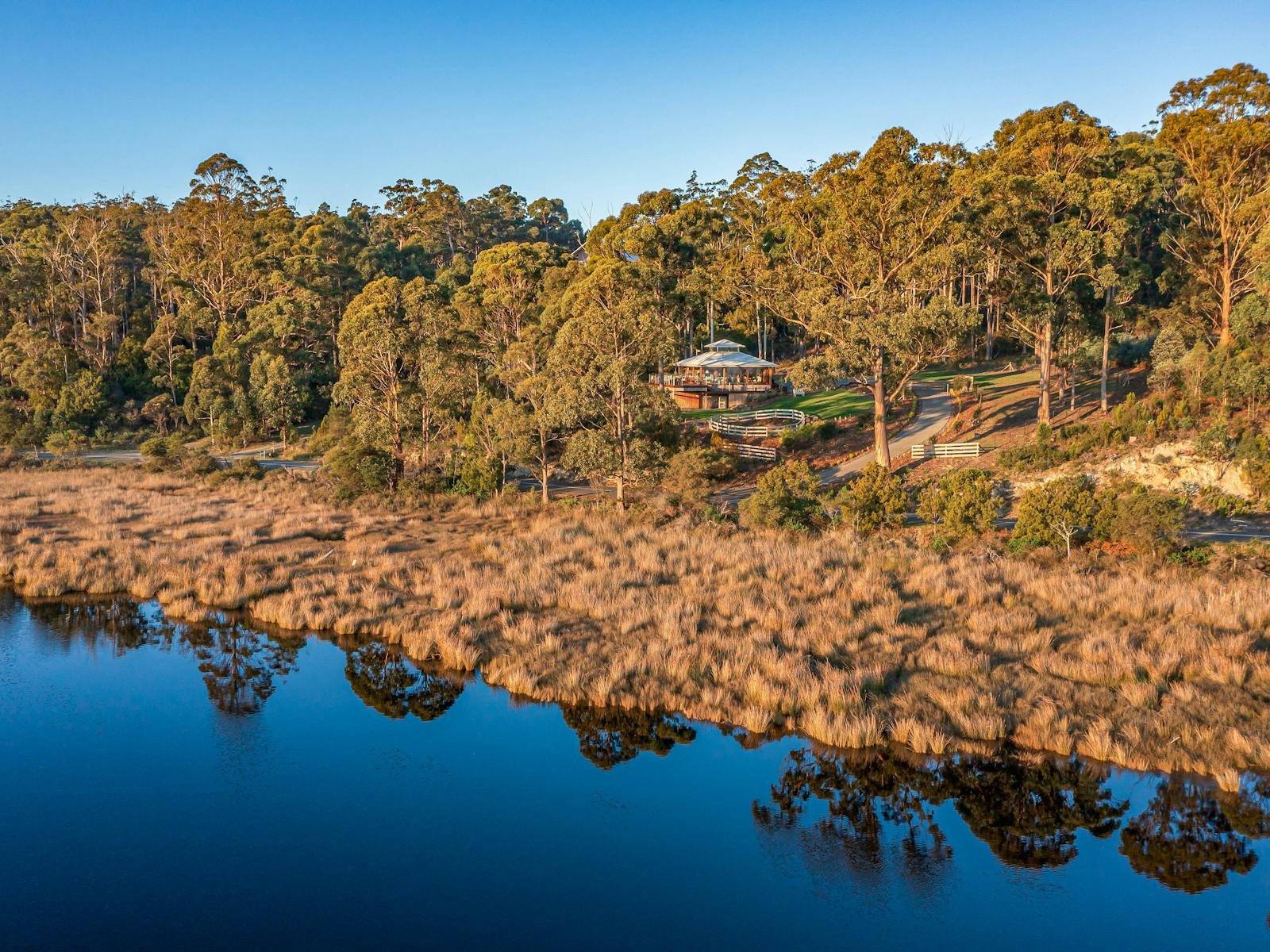 A panoramic drone shot of the Huon River Hideaway property take from above a reflective Huon River