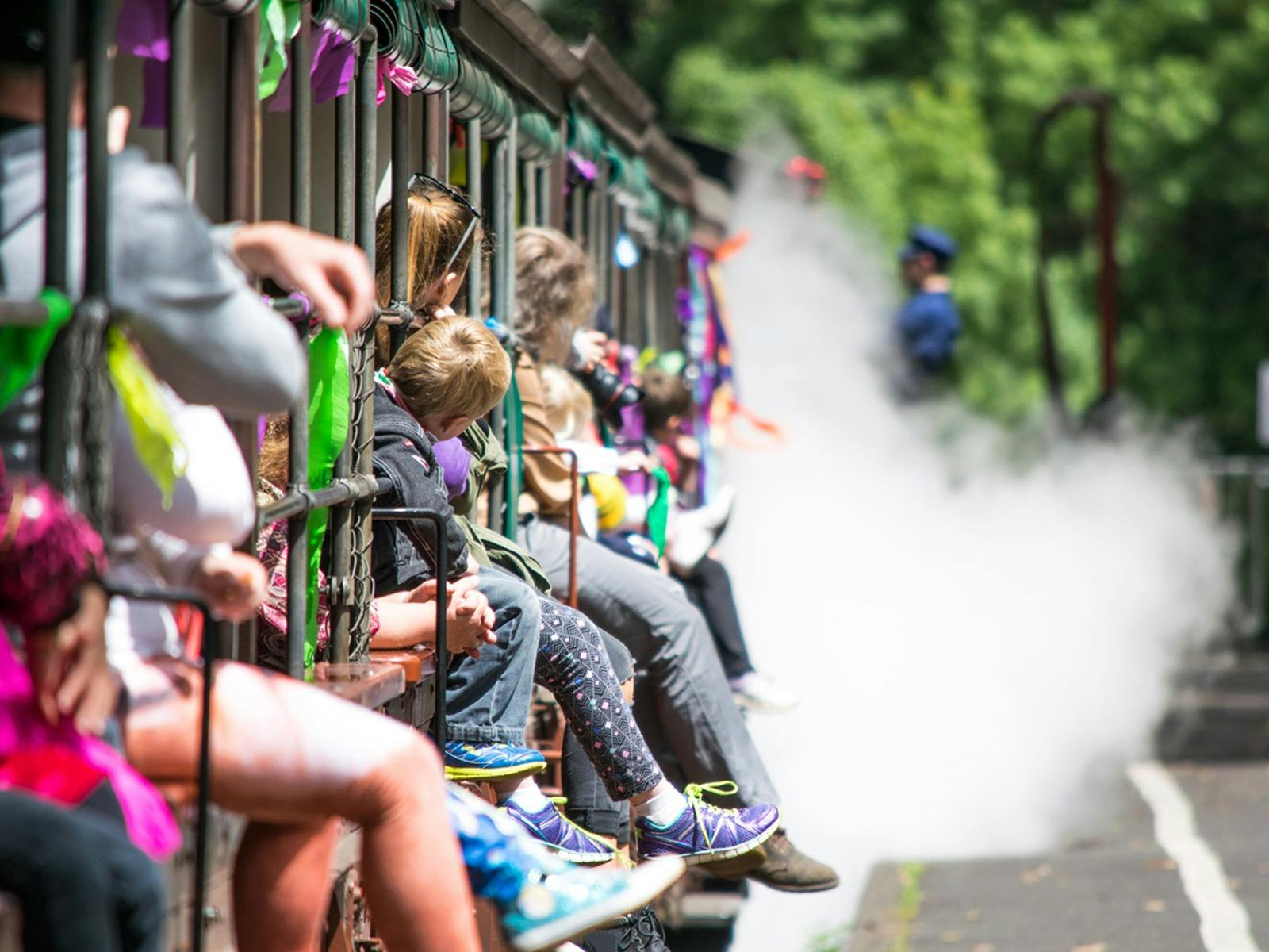 Children and adults sitting on the window sill with legs dangling out of Puffing Billy steam train