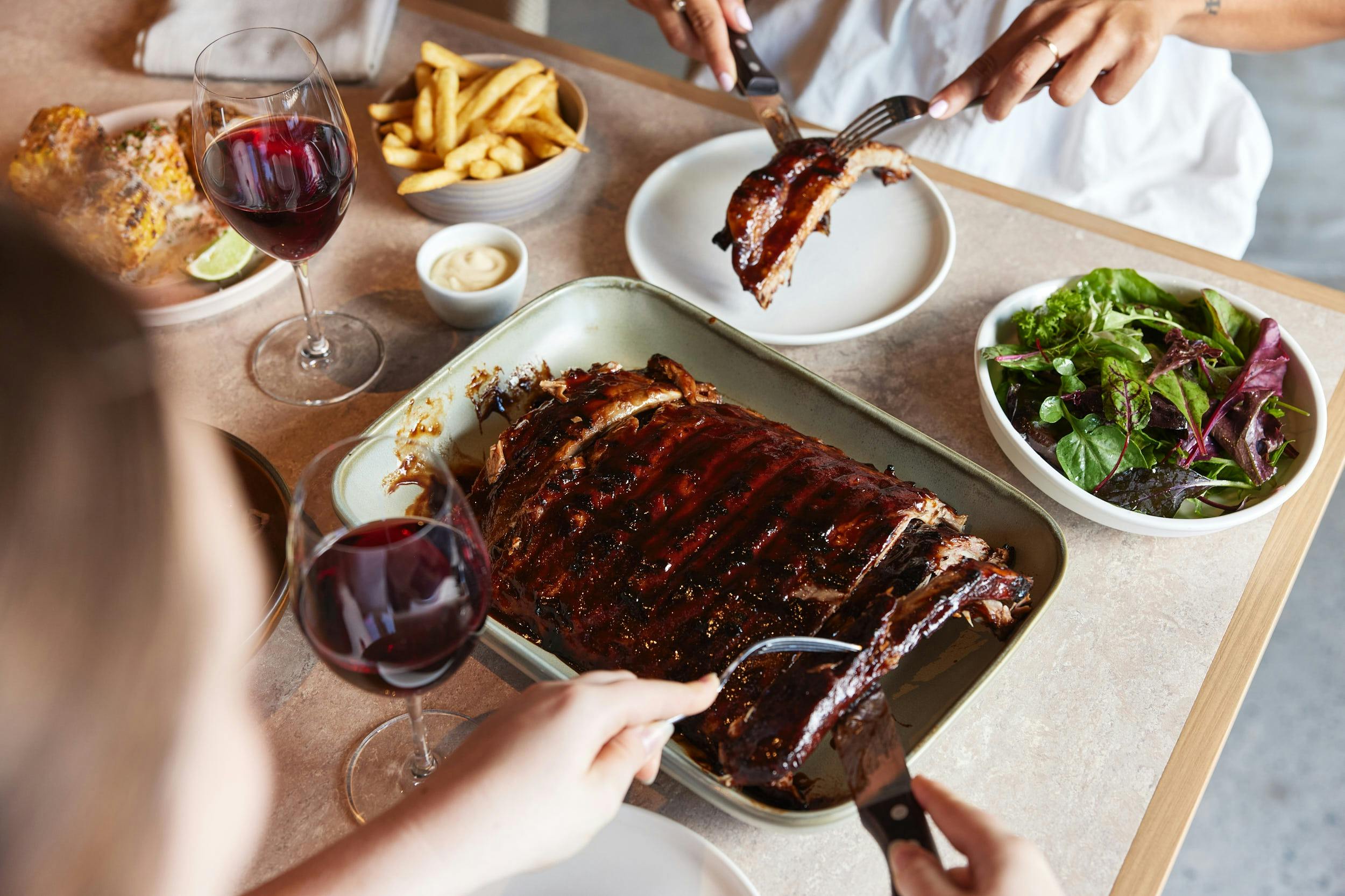 Full rack of pork ribs with fries and salad on the side paired with a glass of wine