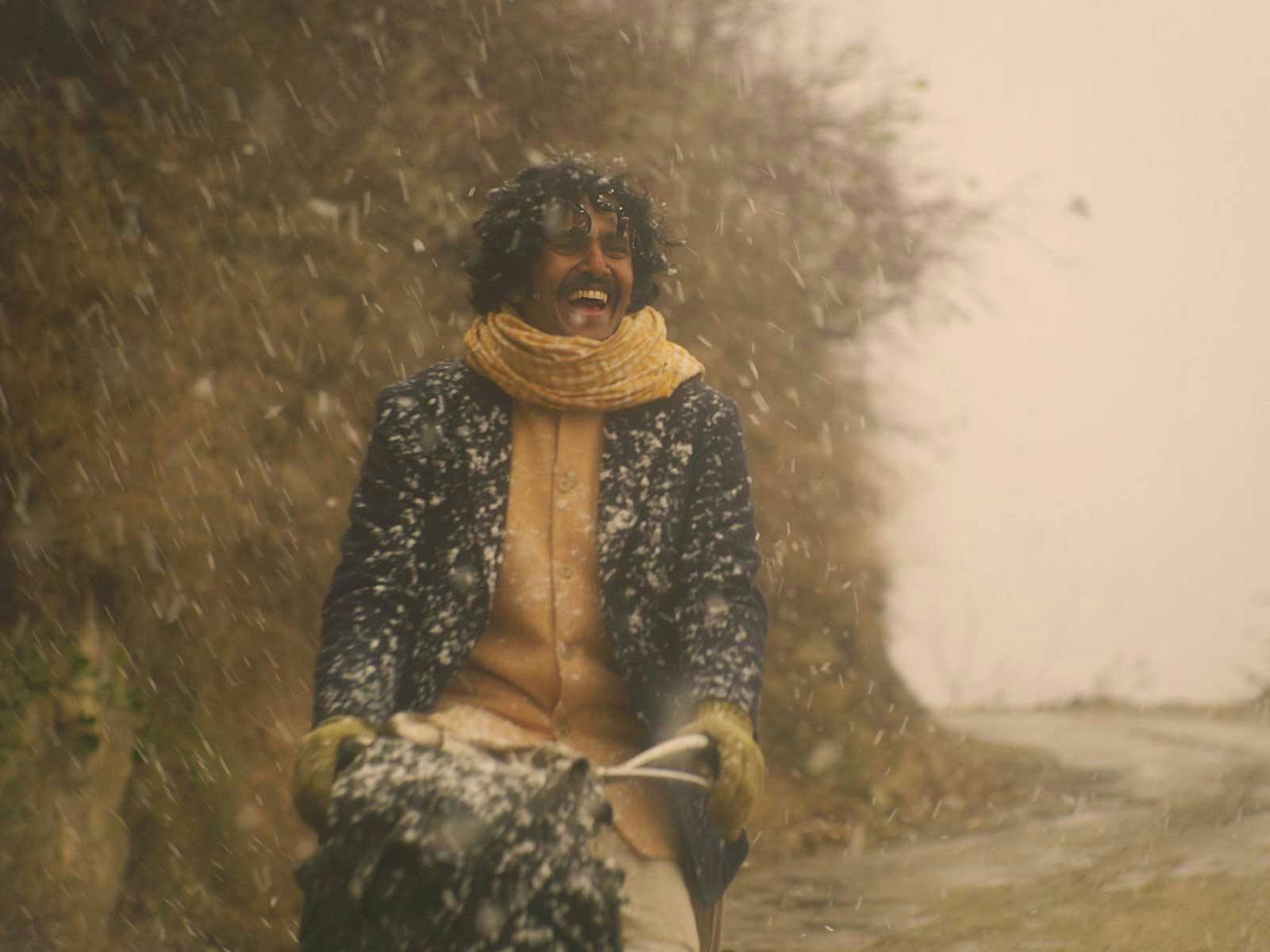 A smiling man, rides a bike through falling snow