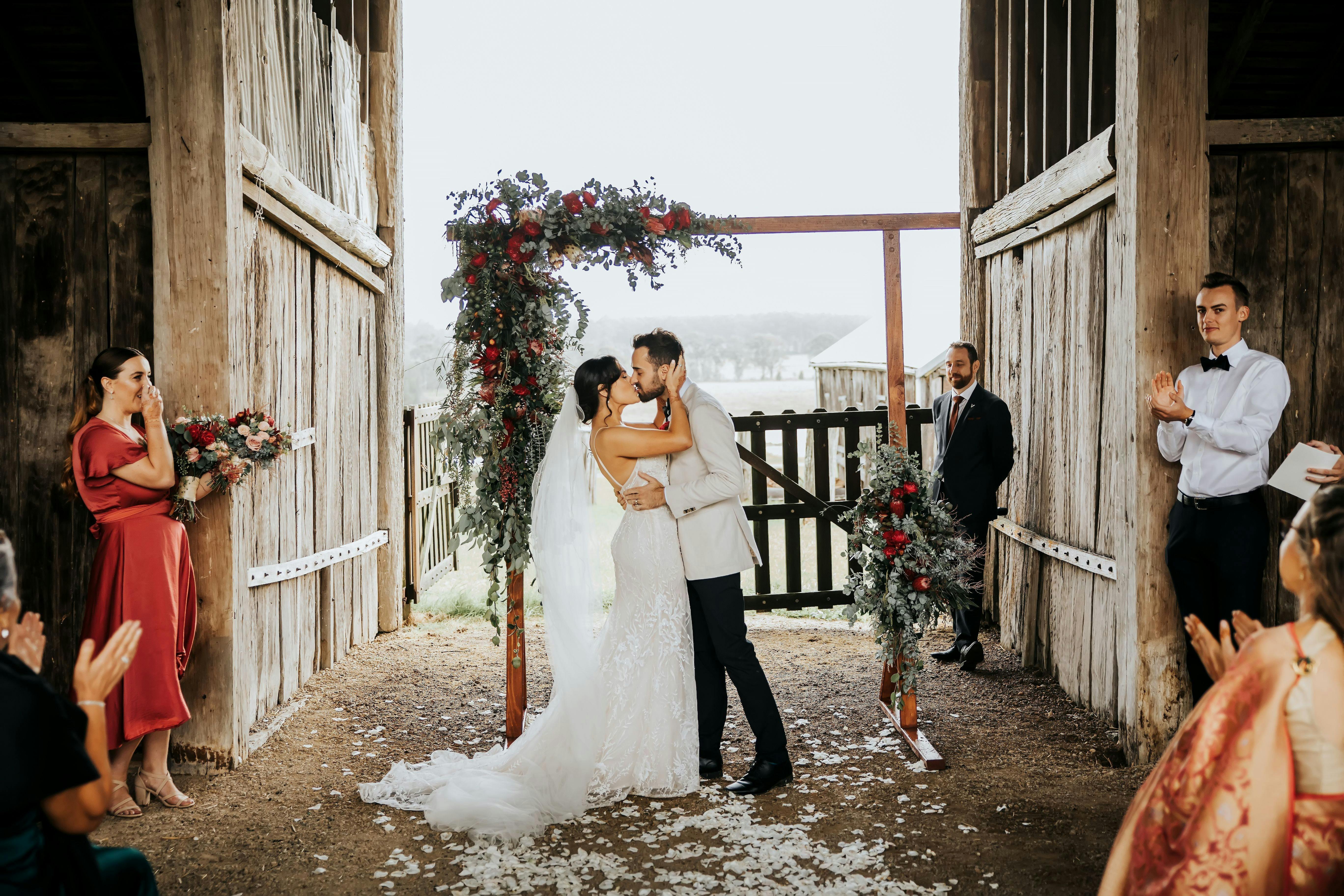 Bride and groom kissing in wet weather barn