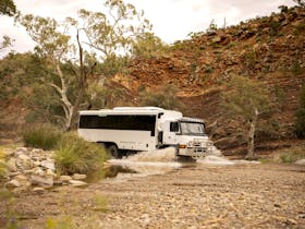 6WD coach splashing through water as it drives through a gorge