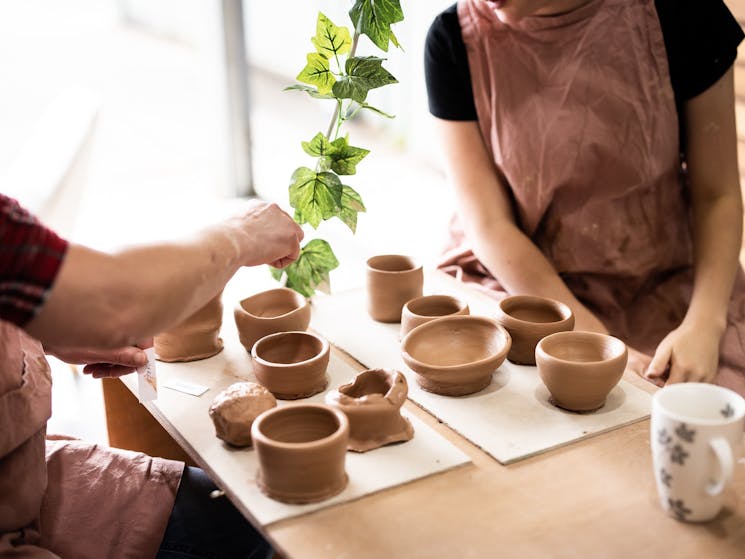 Picture of two people and finished clay pots on  a bench