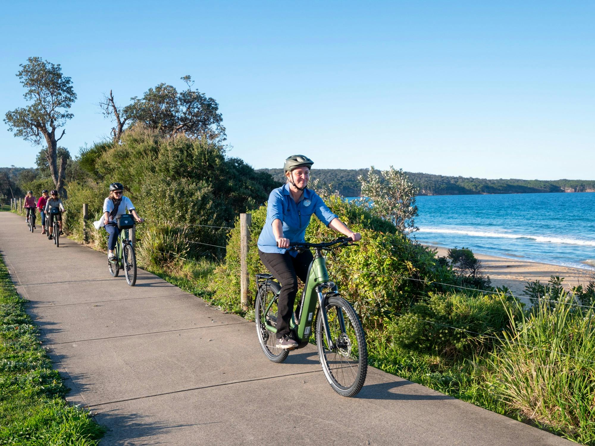 Guide and guests cycling along a dedicated cycle pathway with beach in background, Eden