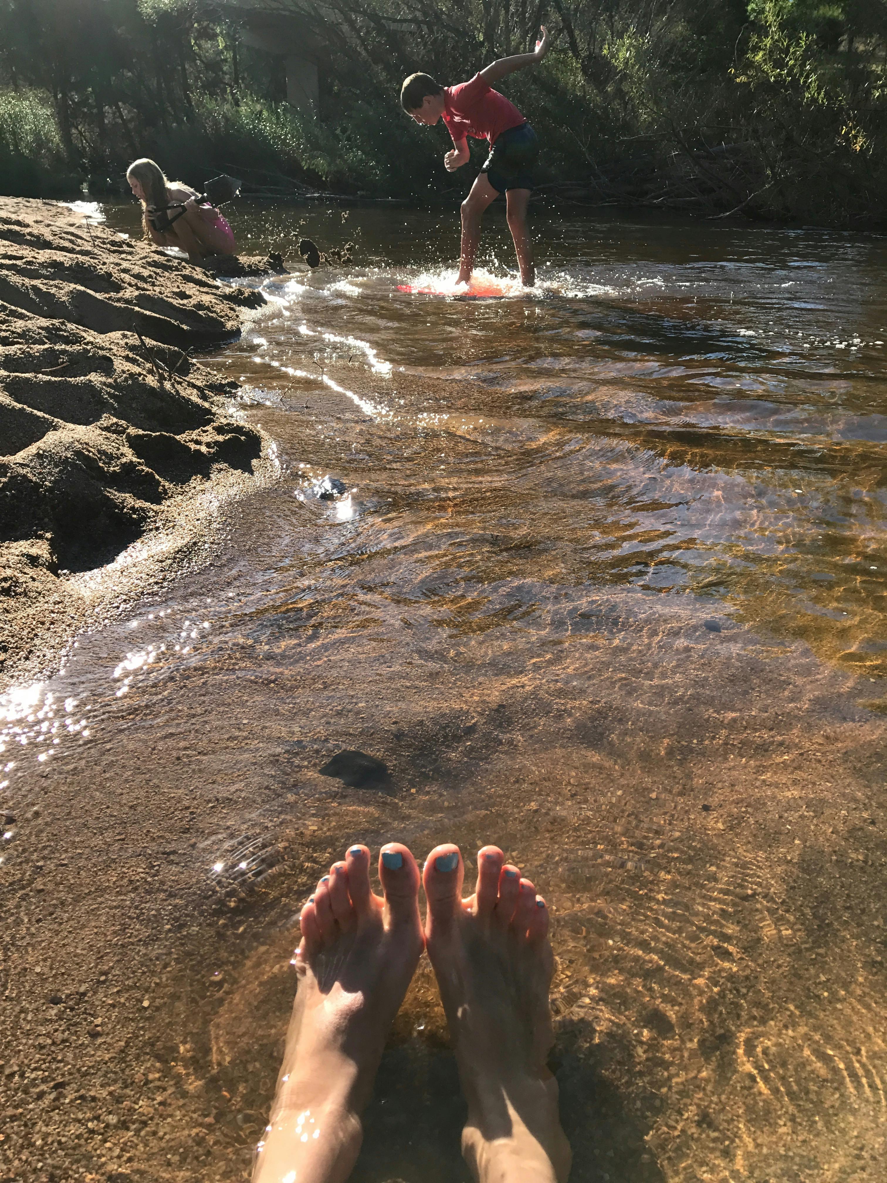 feet in the foreground, sun sparkling on water, kids playing