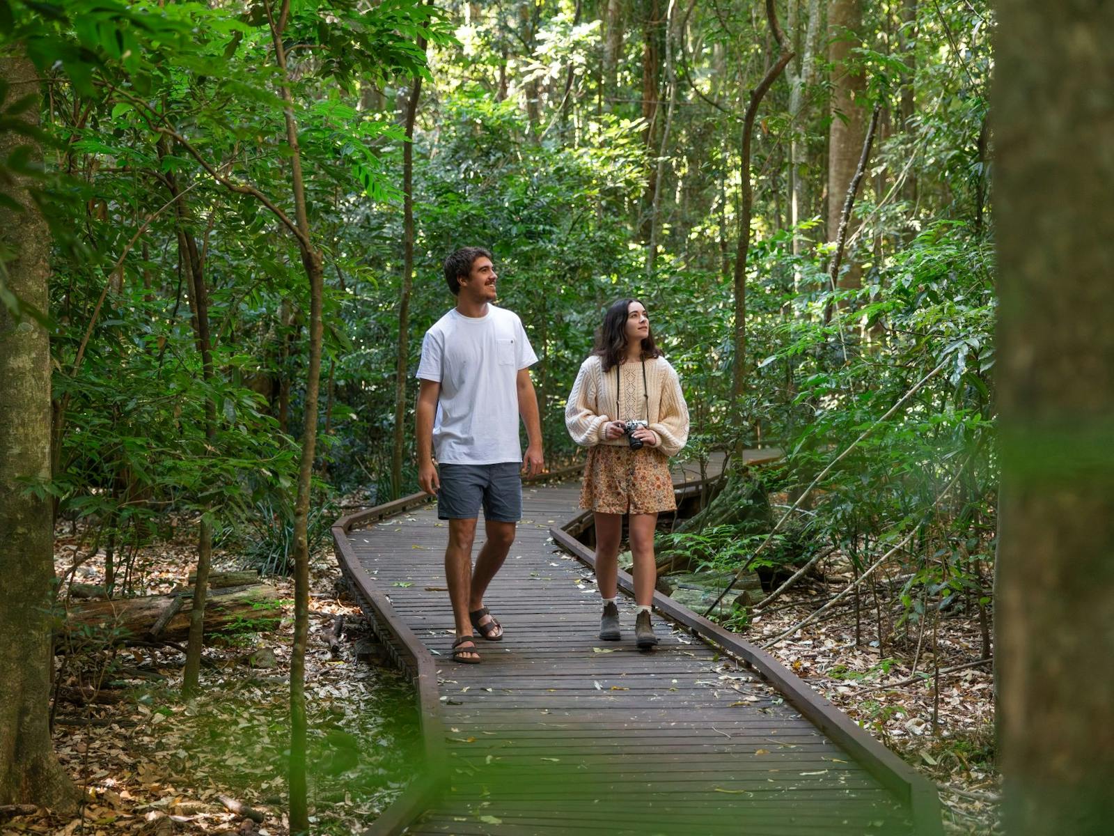 couple walking along wooden boardwalk surrounded by forest