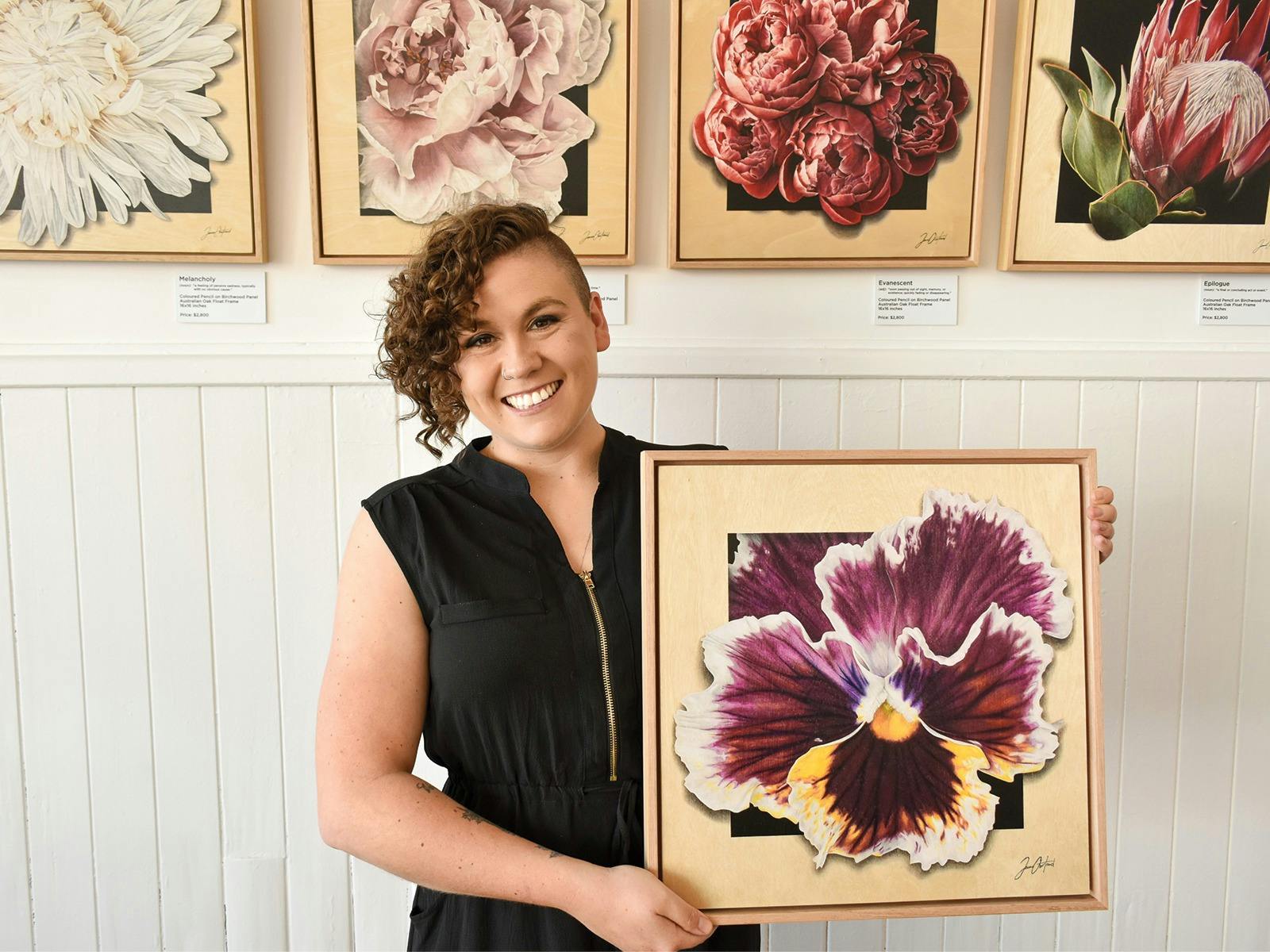 The artist is holding her artwork up, which is a pansy drawn on birchwood panel.