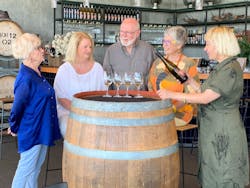 5 people standing around a wine barrel tasting wine