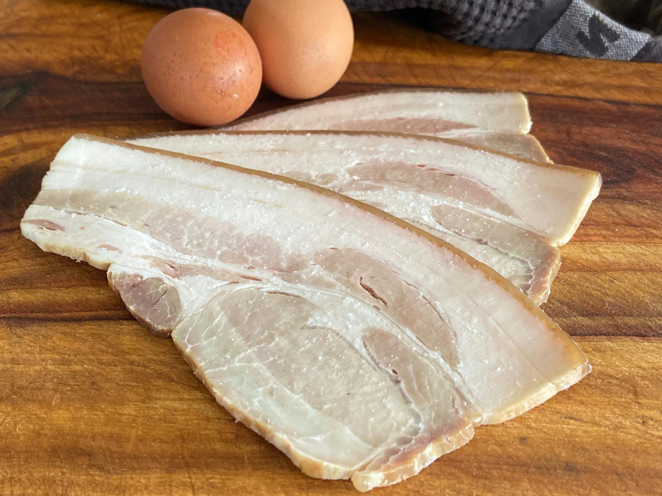 Nitrate-free pasture raised Bershire bacon slices displayed on a wooden board with eggs.