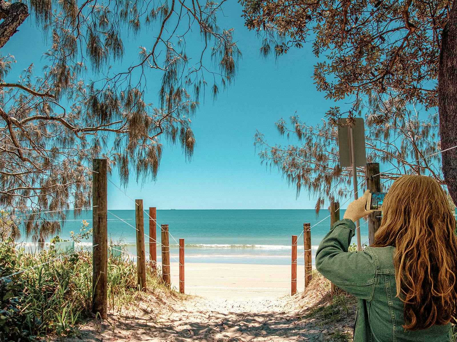 Looking down a Mooloolaba Beach walkway to the water, with a girl taking a photo on her smartphone. Looking down a Mooloolaba Beach walkway to the water, with a girl taking a photo on her smartphone.