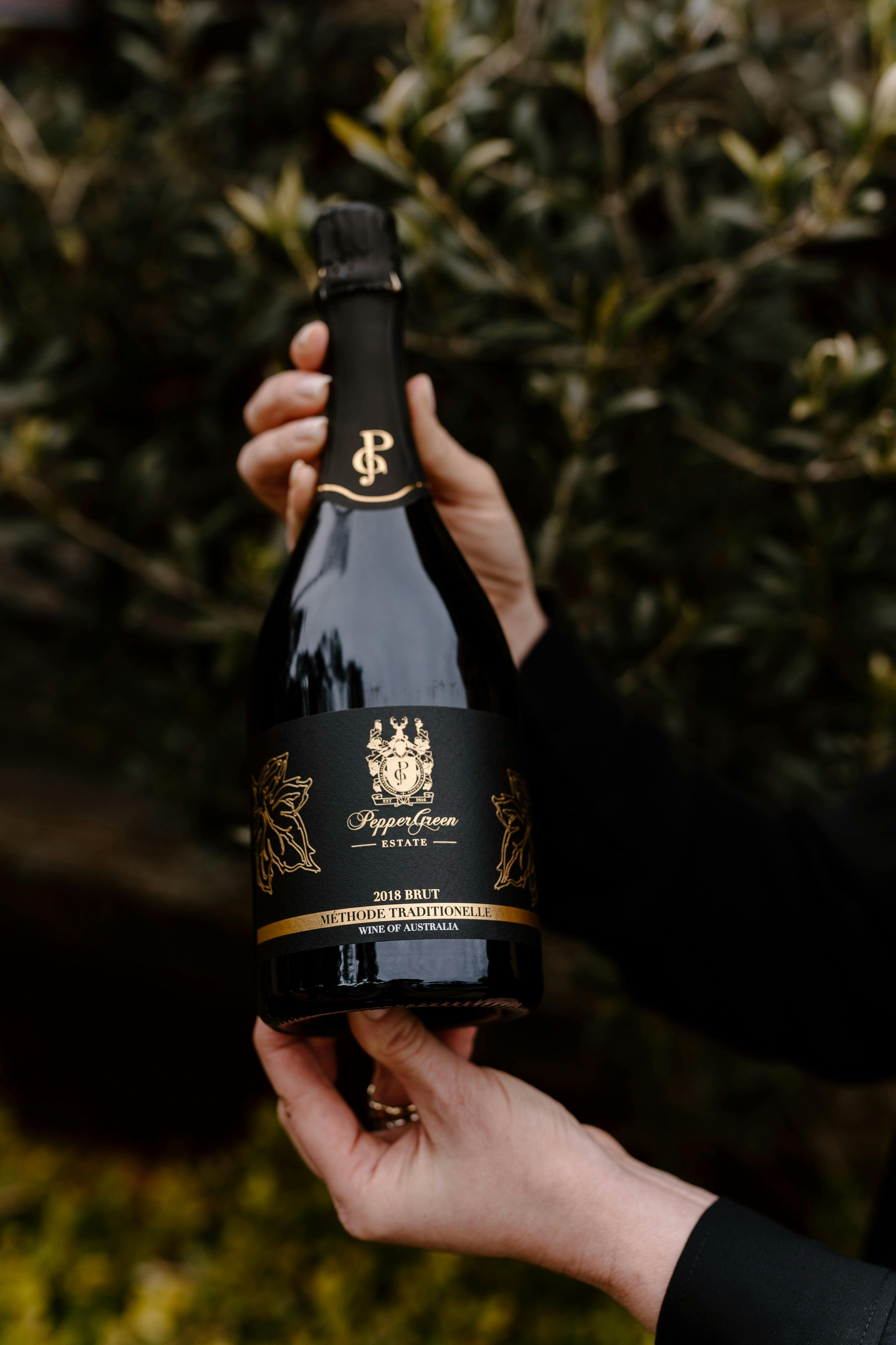 A woman's hand holding a bottle of 2018 Brut Méthode Traditionelle Sparkling Wine