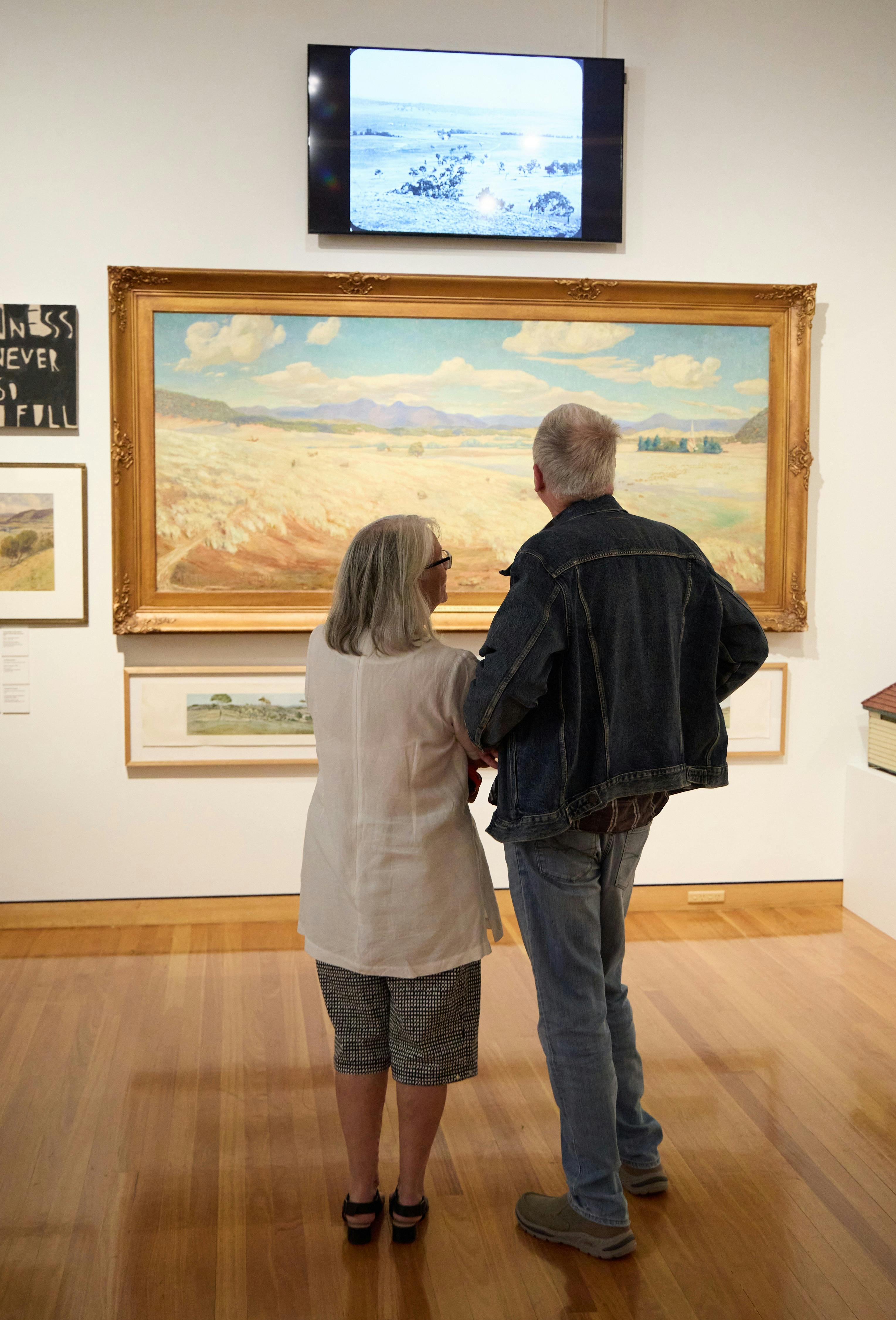Visitors observing a landscape painting in the Canberra/Kamberri exhibition