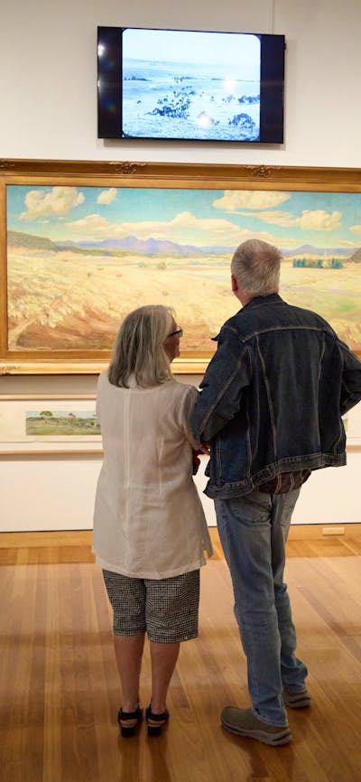 Visitors observing a landscape painting in the Canberra/Kamberri exhibition