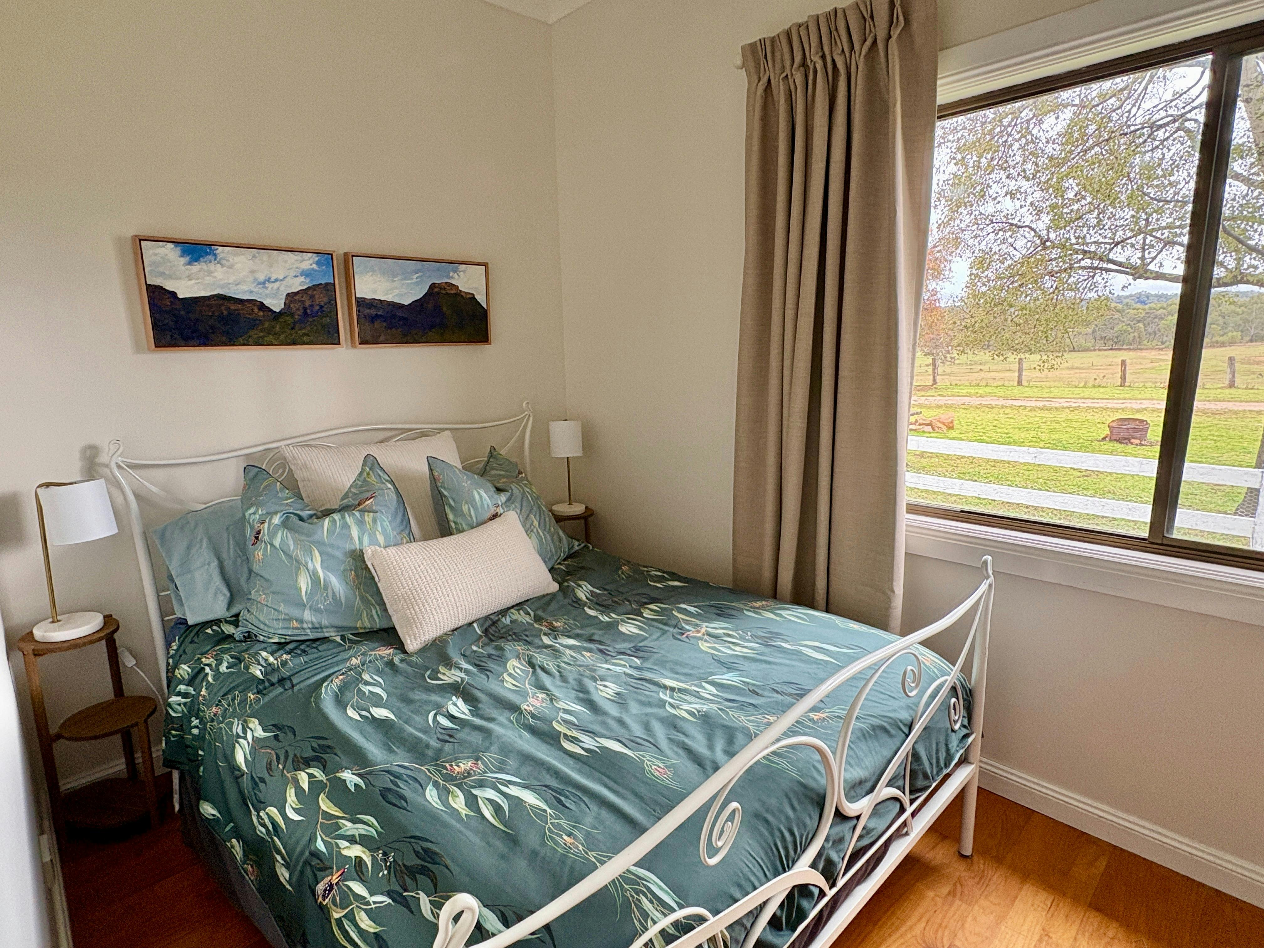 White steel bed with green bed covers in farm cottage in Capertee Valley