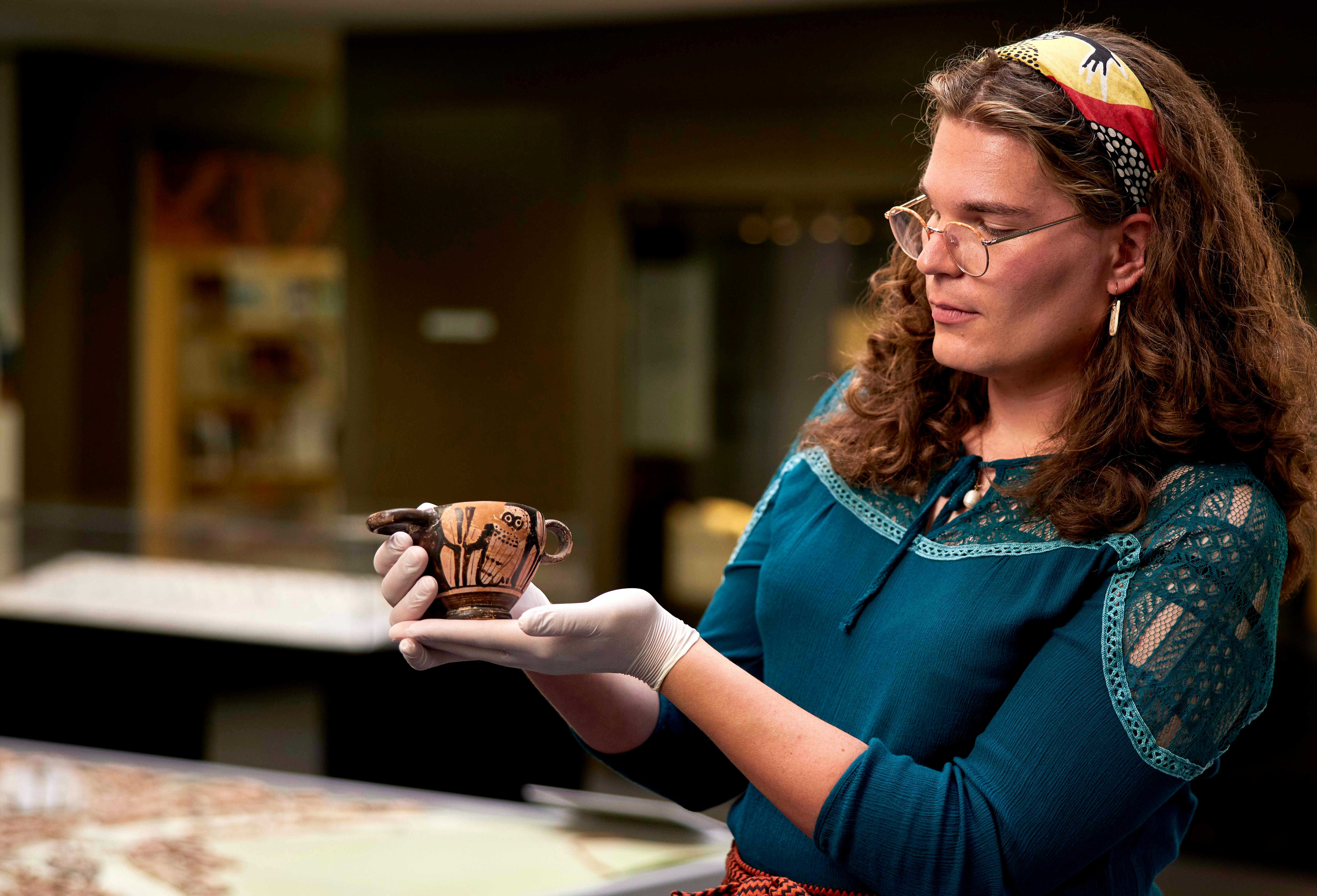 Tour attendee handling a small ceramic object with latext gloves on