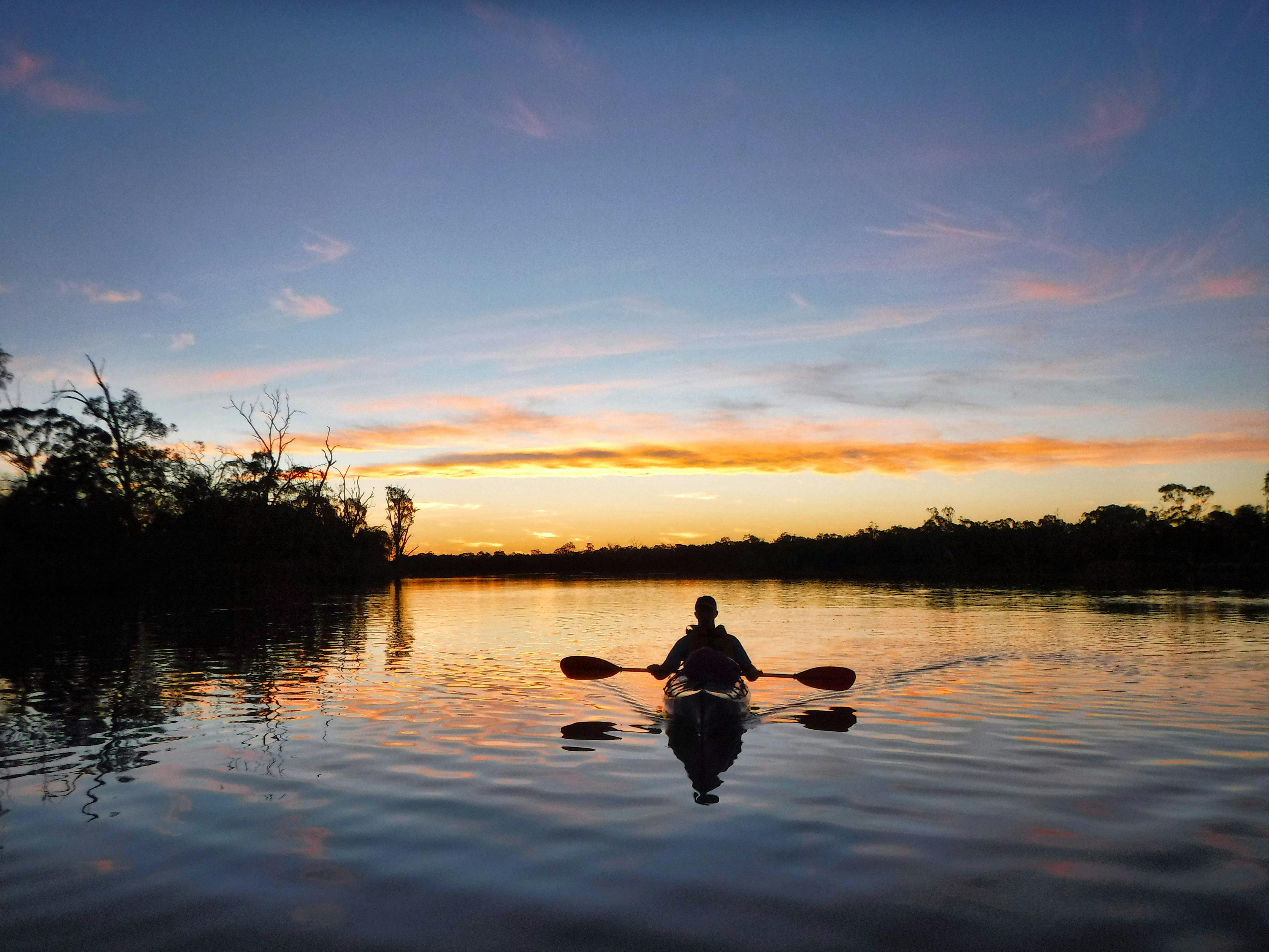 Kayaker on calm waters silhouetted against a a colourful sunset