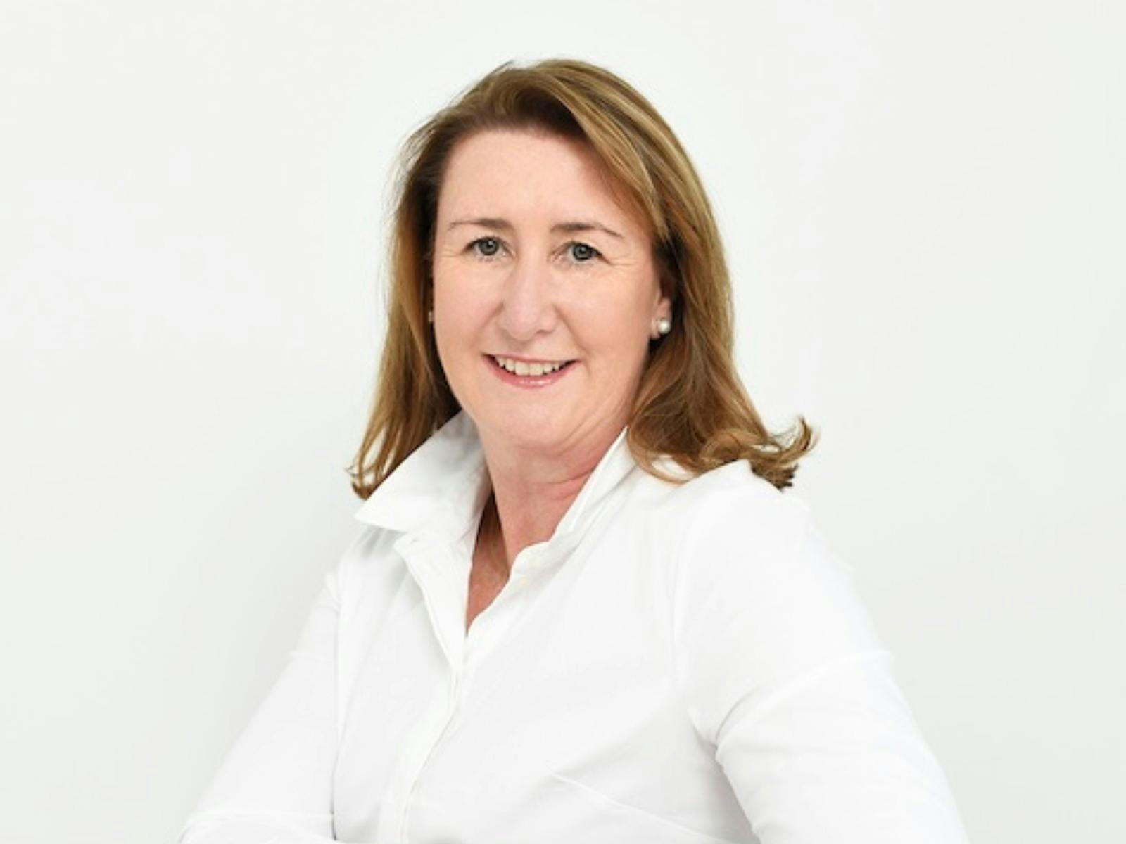 A smiling woman with shoulder-length brown hair, wearing a white collared shirt.