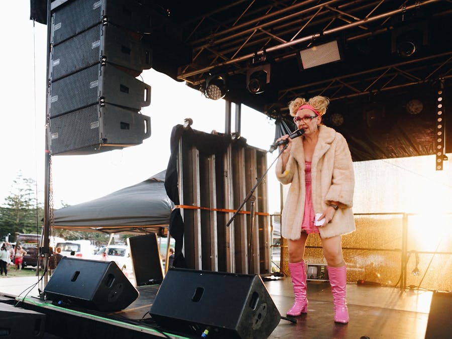 Female comedian on microphone dressed in pink with a jacket on and hair in two buns