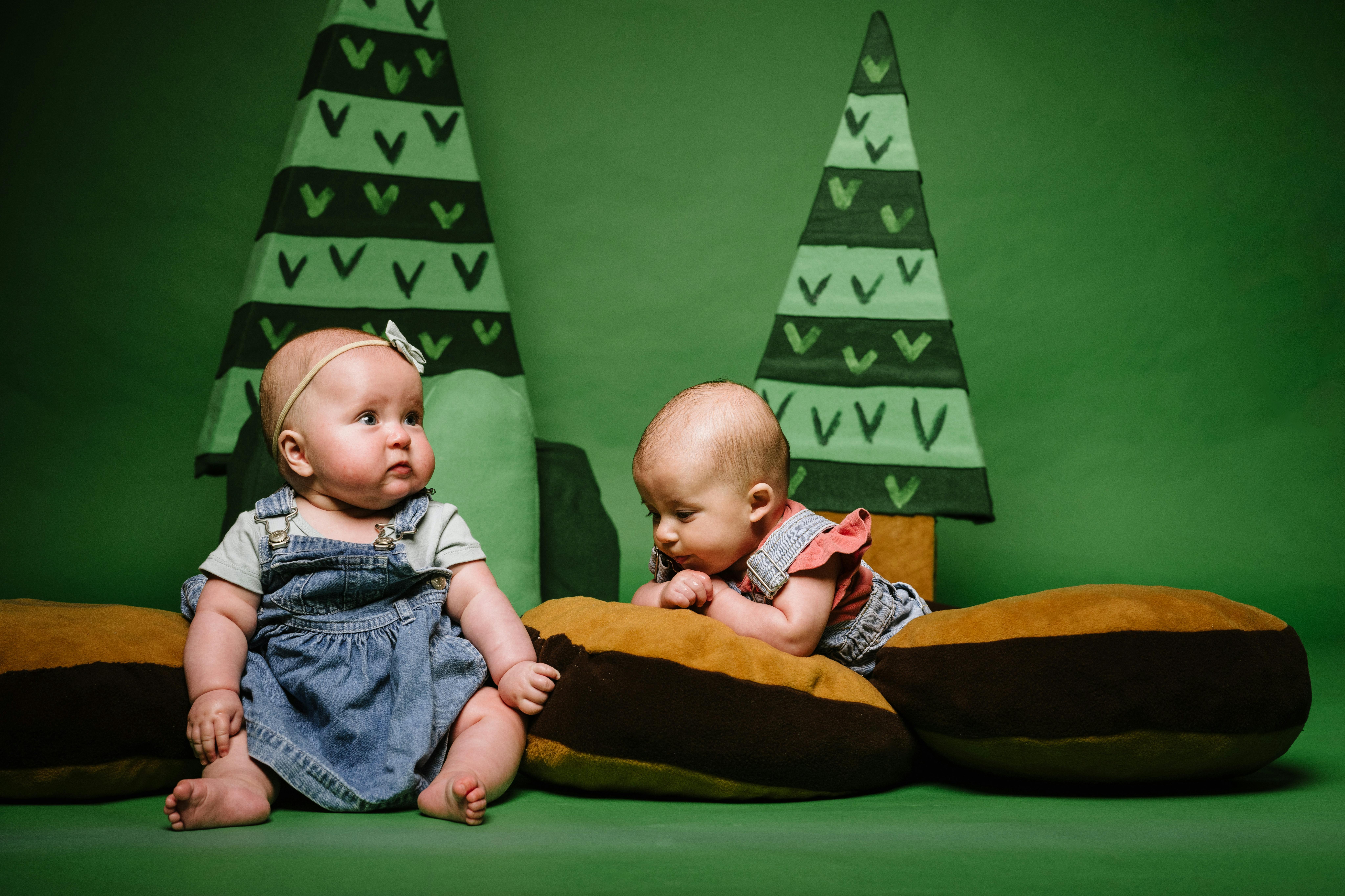 Two babies sitting and playing in front of a paper forest background
