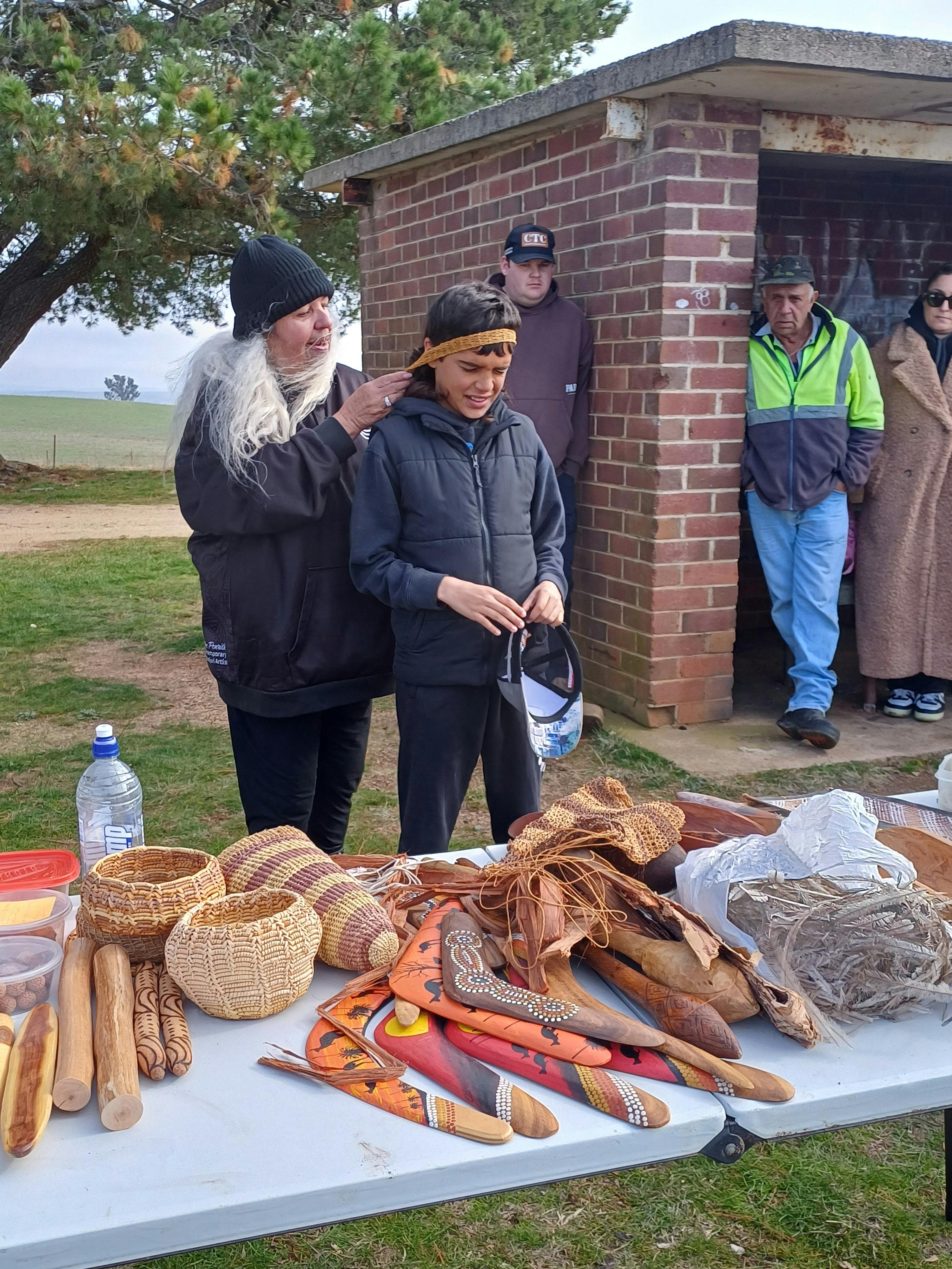 エニッドおばさんがツアー参加者の頭に運搬用具の柄を巻き付けている。