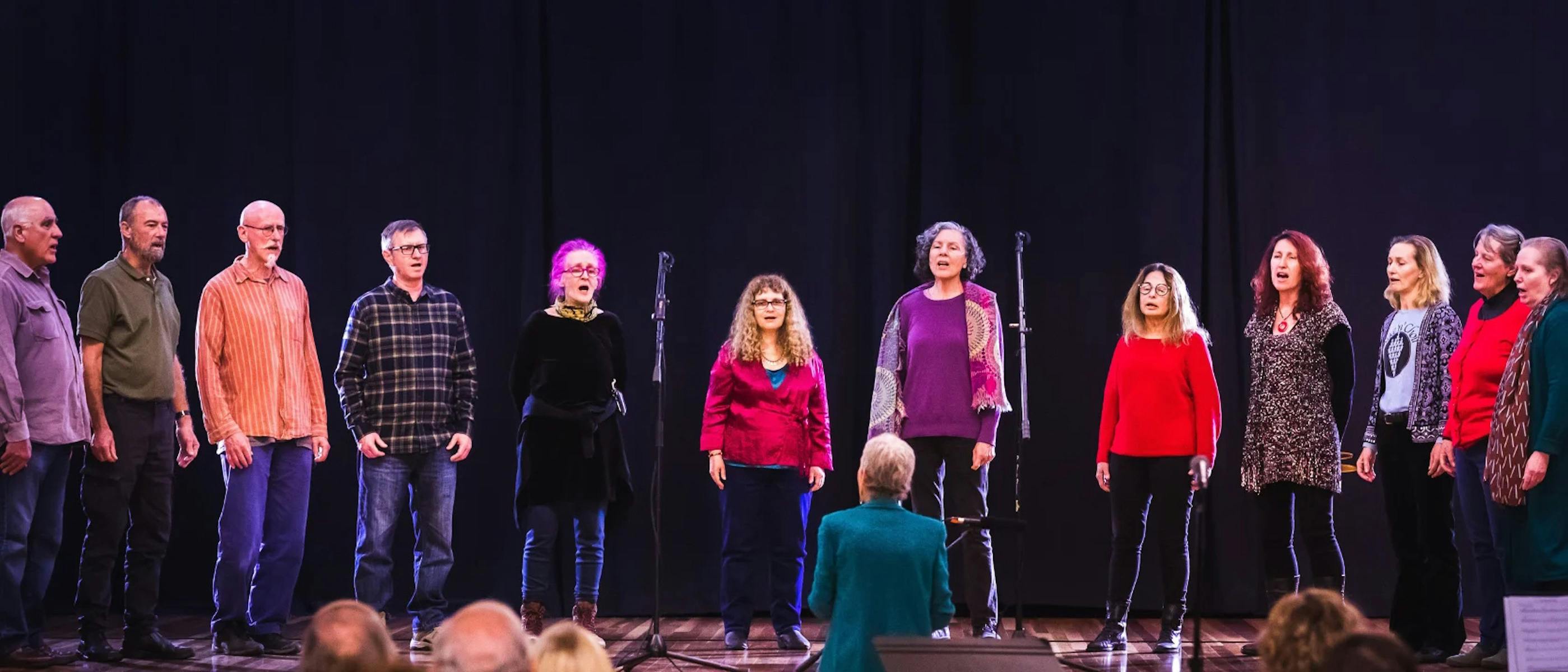 A group of singers dressed in casual clothing stand on stage