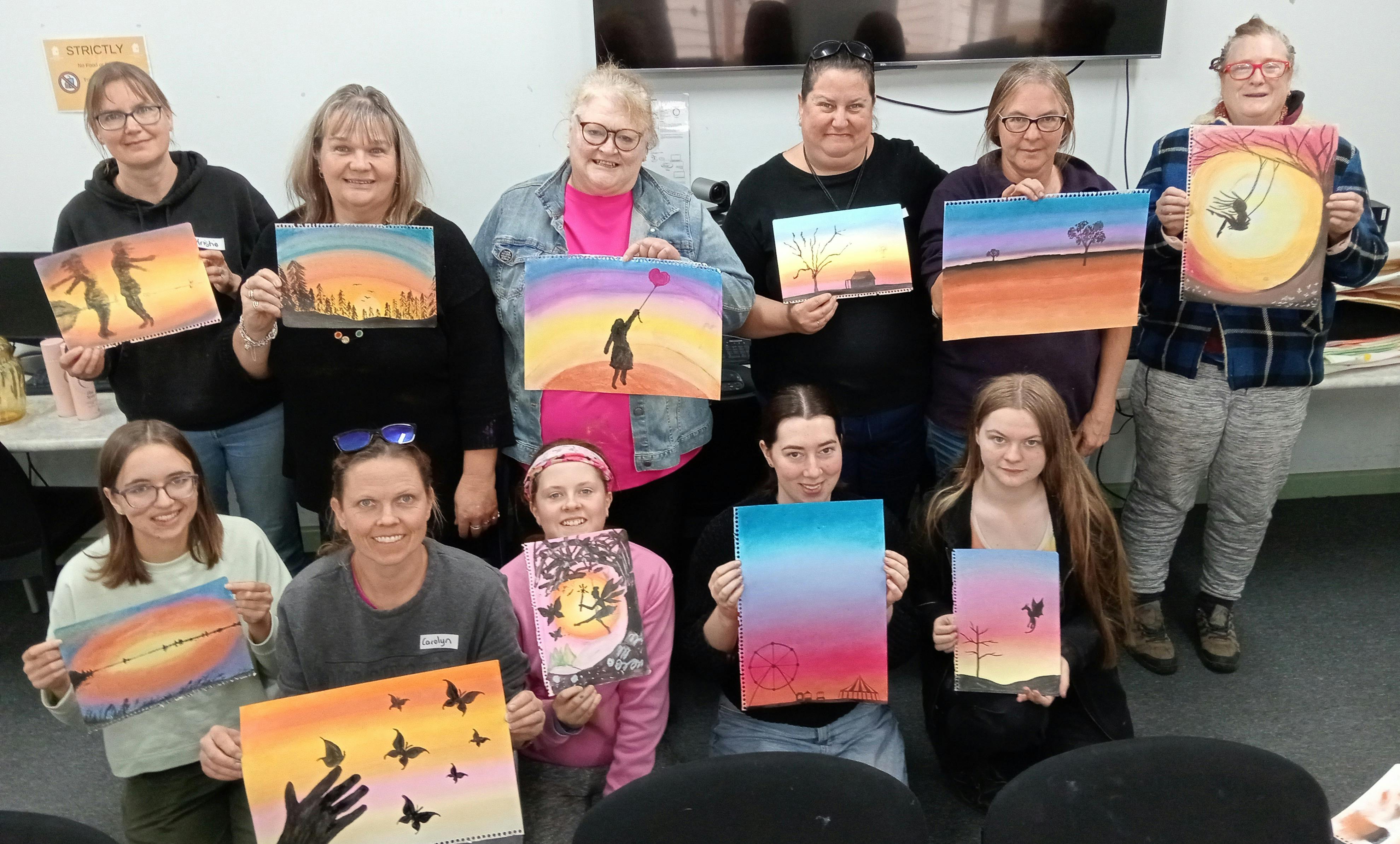 Pastel Art Class at Pax Art Studio ladies holding colourful artworks of sunsets