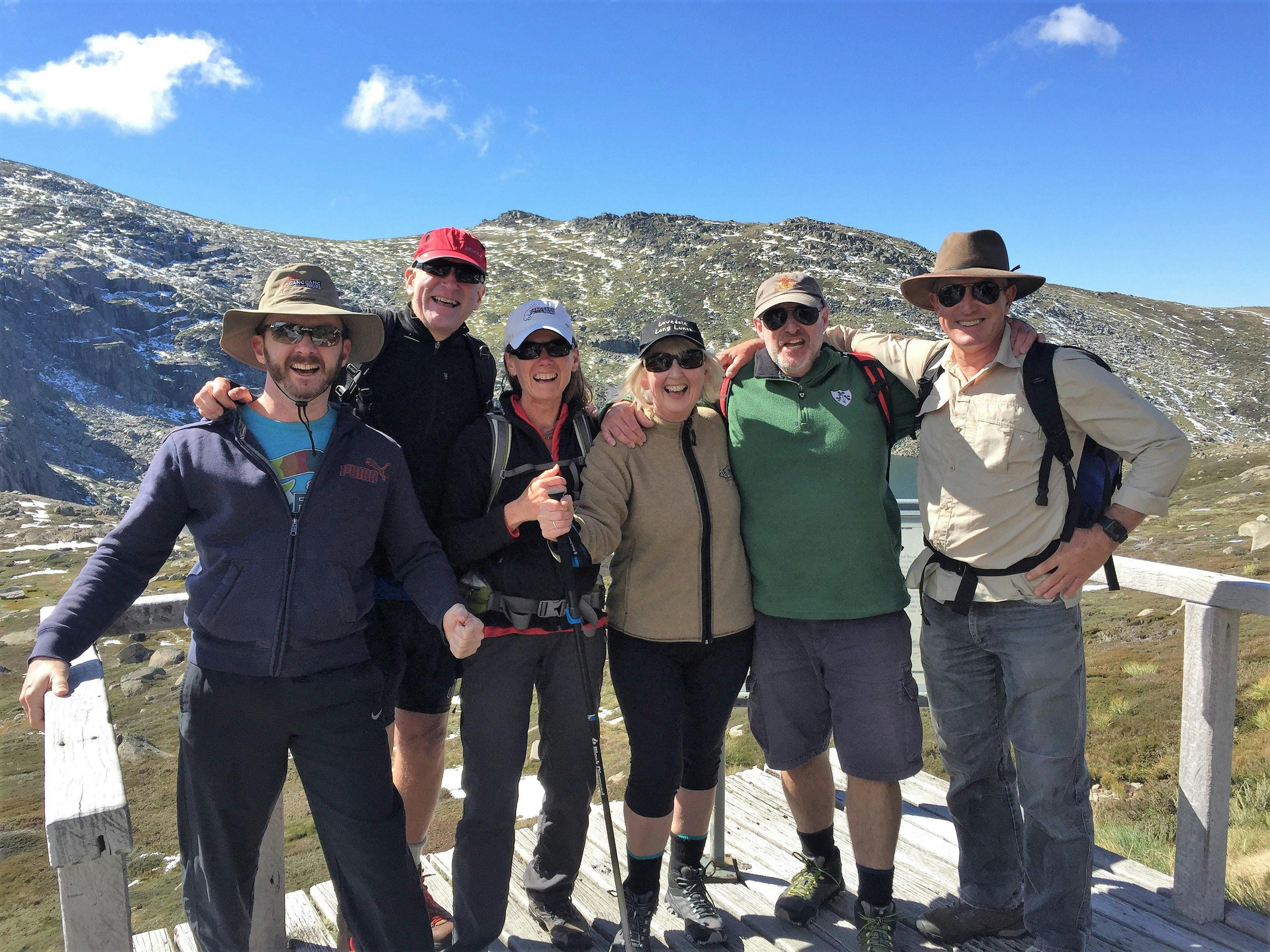 6 adults standing on platform in from of lake and mountains