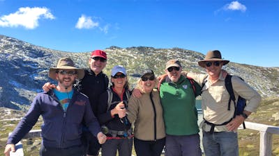 6 adults standing on platform in from of lake and mountains