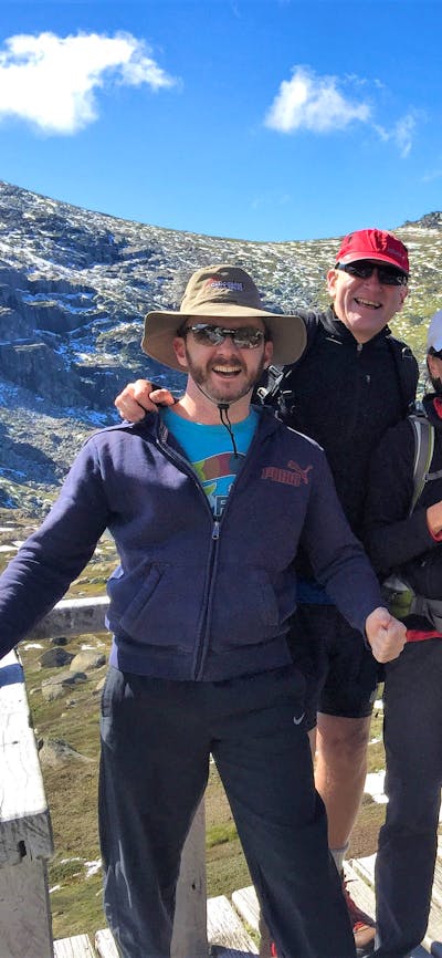 6 adults standing on platform in from of lake and mountains