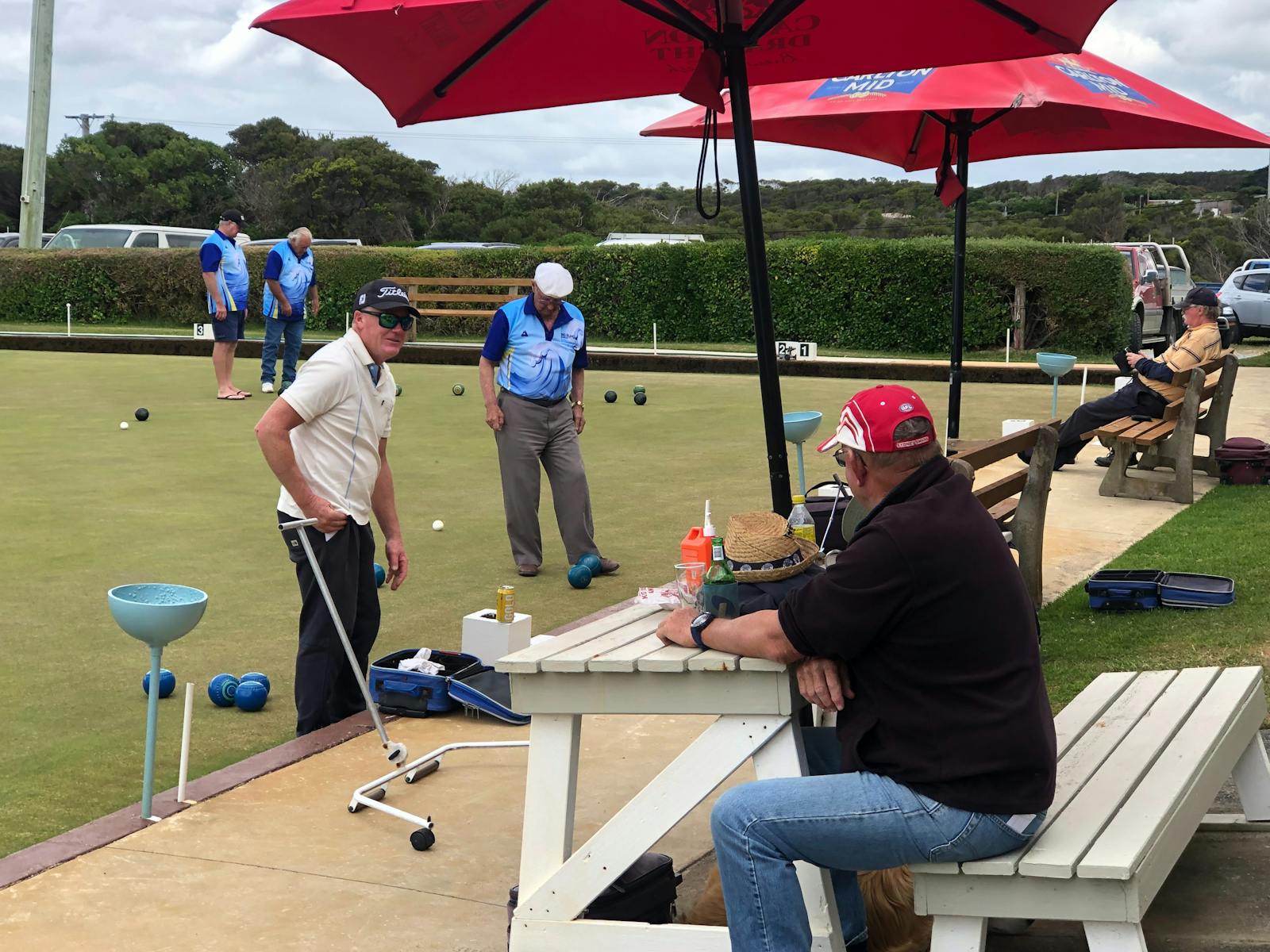 Photo of bowlers playing with spectators sitting under umbrellas watching