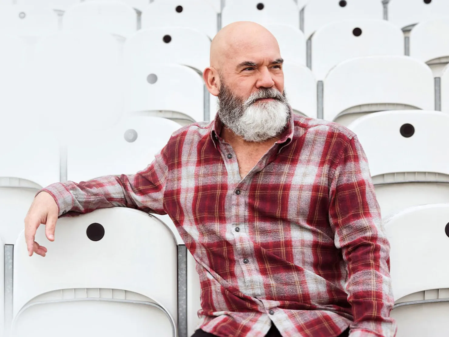 Marty seating in stadium seating with left arm over the next chair in maroon checked shirt