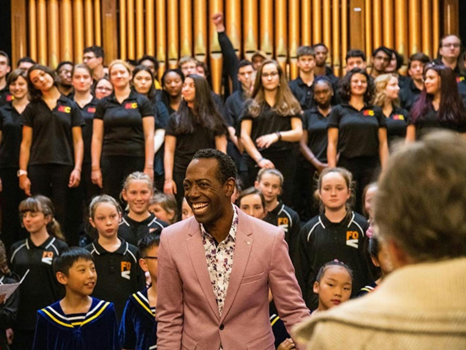 man in pink jacket smiling with choir in background