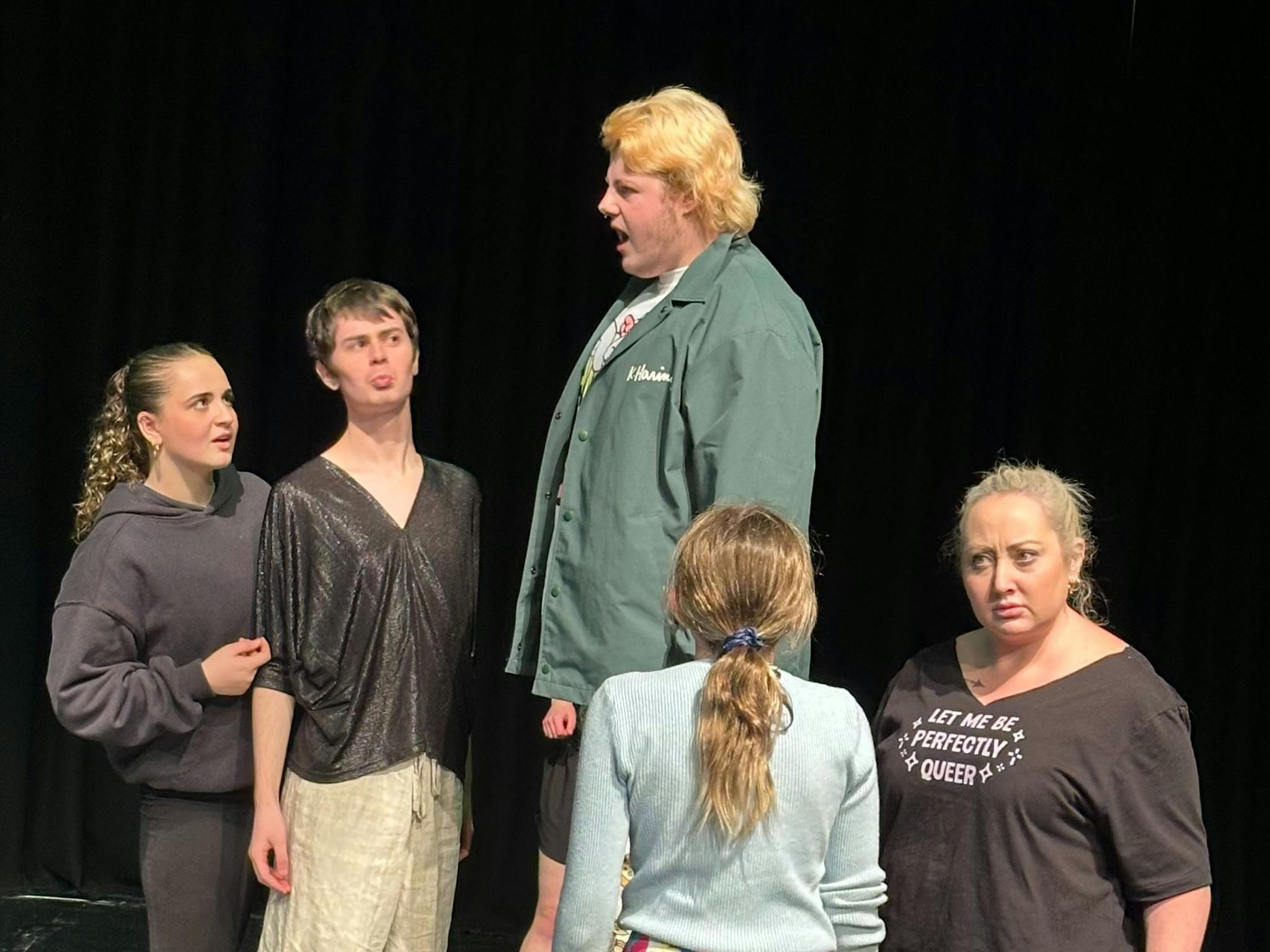 Tobias standing on a platform singing to people (ensemble) in the marketplace