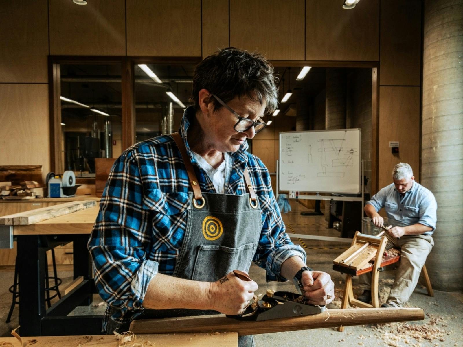 Two people shaving wood inside workshop