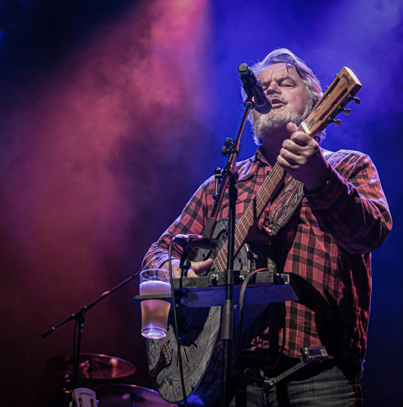A man standing behind a microphone singing and playing guitar